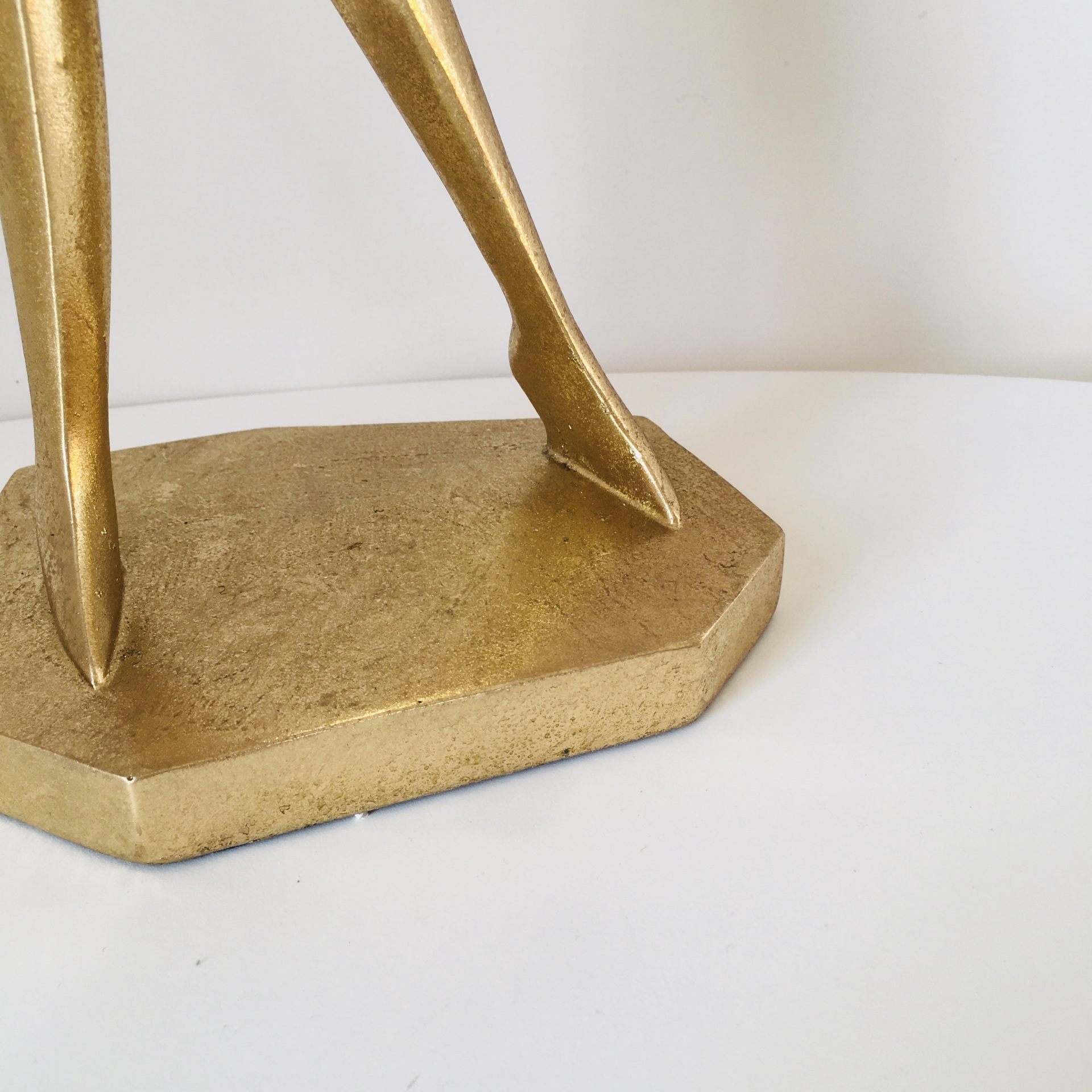 Base e pernas de uma escultura dourada texturizada sobre superfície branca