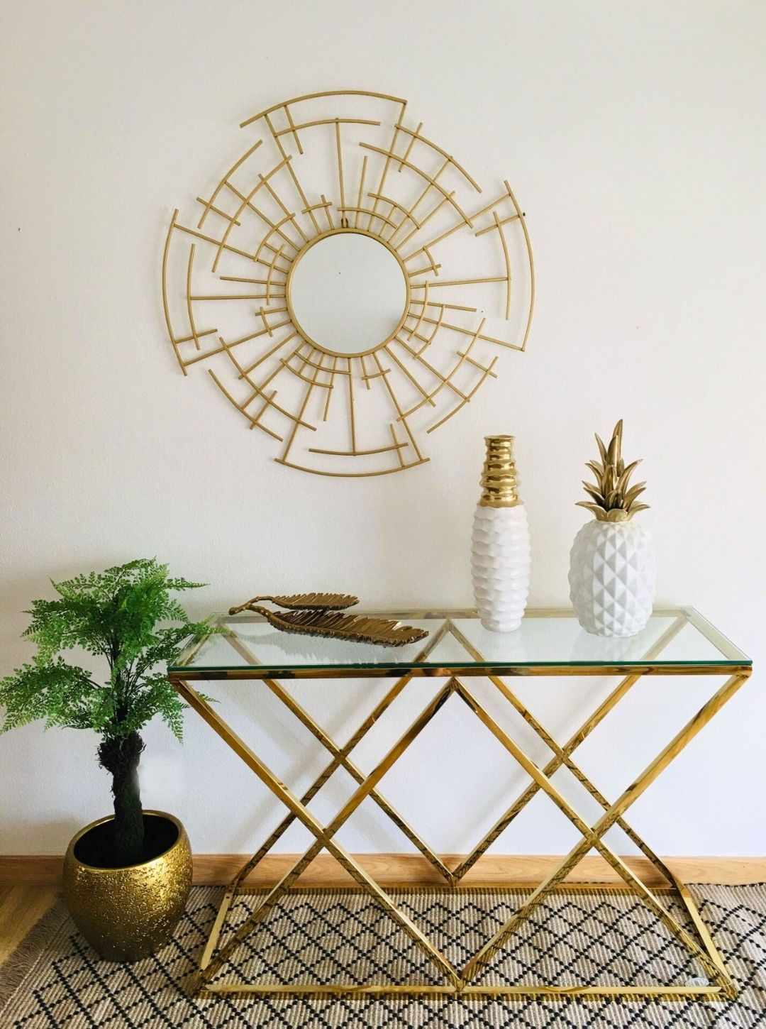 Mesa com tampo de vidro e estrutura dourada decorada com vasos, bandejas, planta em vaso dourado, espelho redondo com moldura metálica dourada na parede
