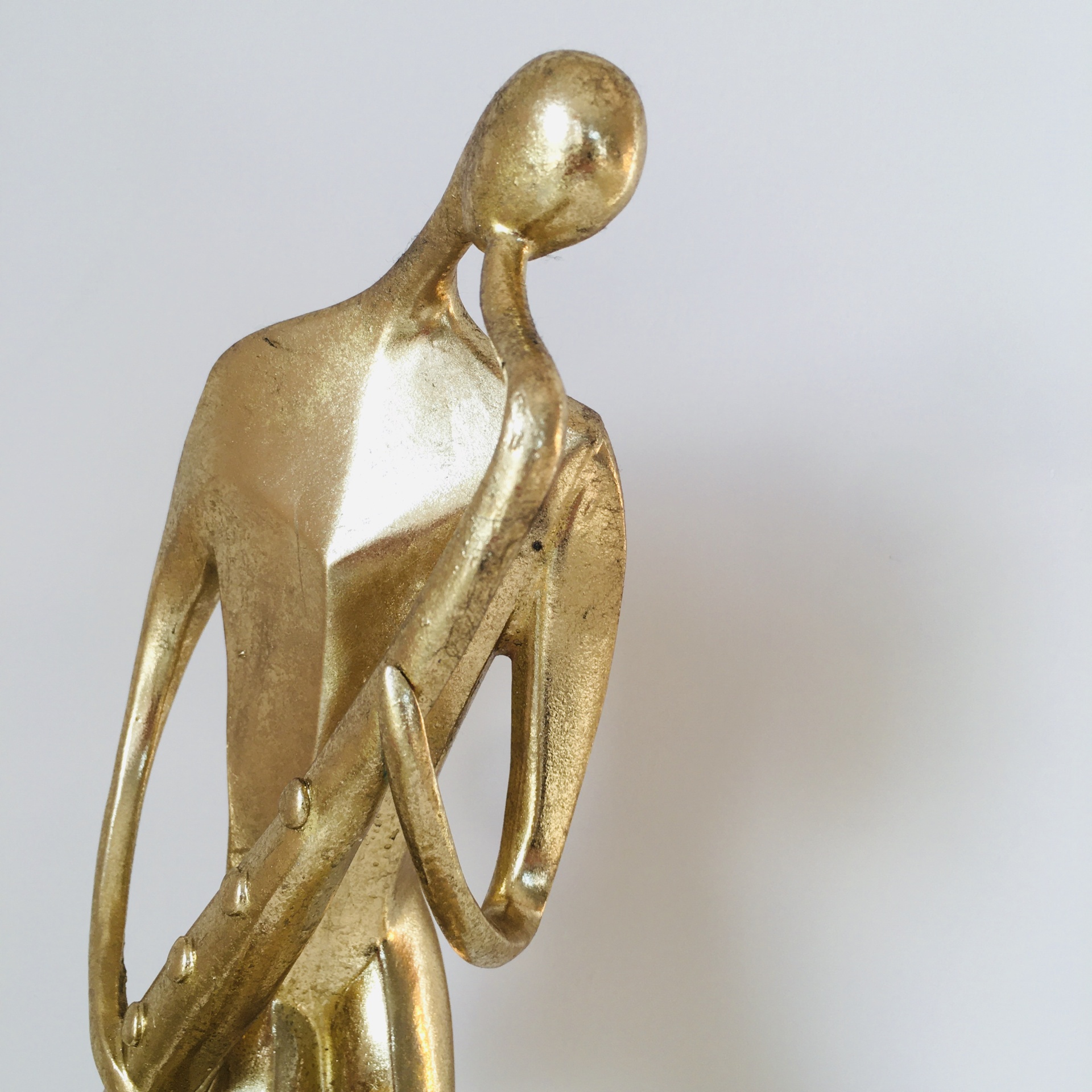 Escultura dourada abstrata de figura humana em pose pensativa