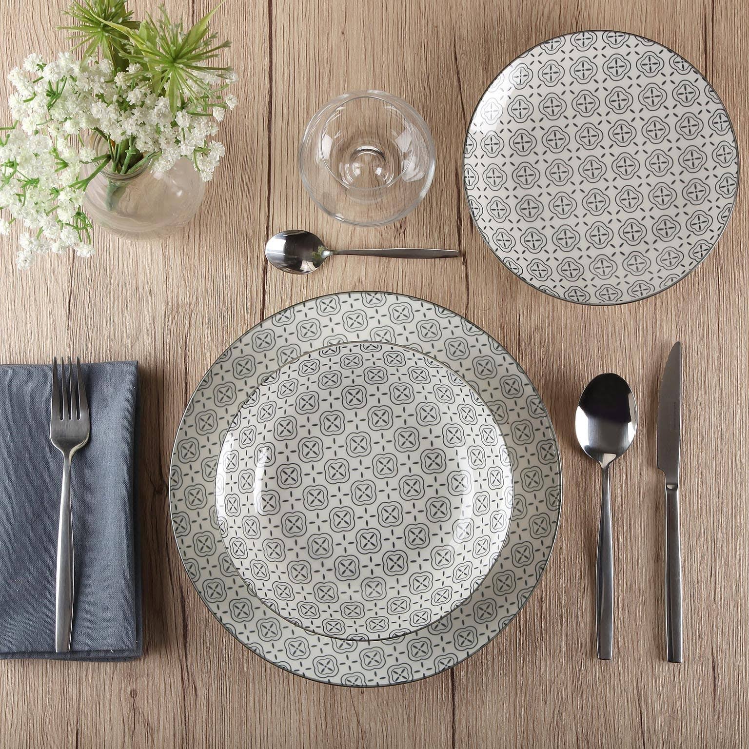 Conjunto de pratos, talheres, copo e vaso com flores brancas numa mesa de madeira clara