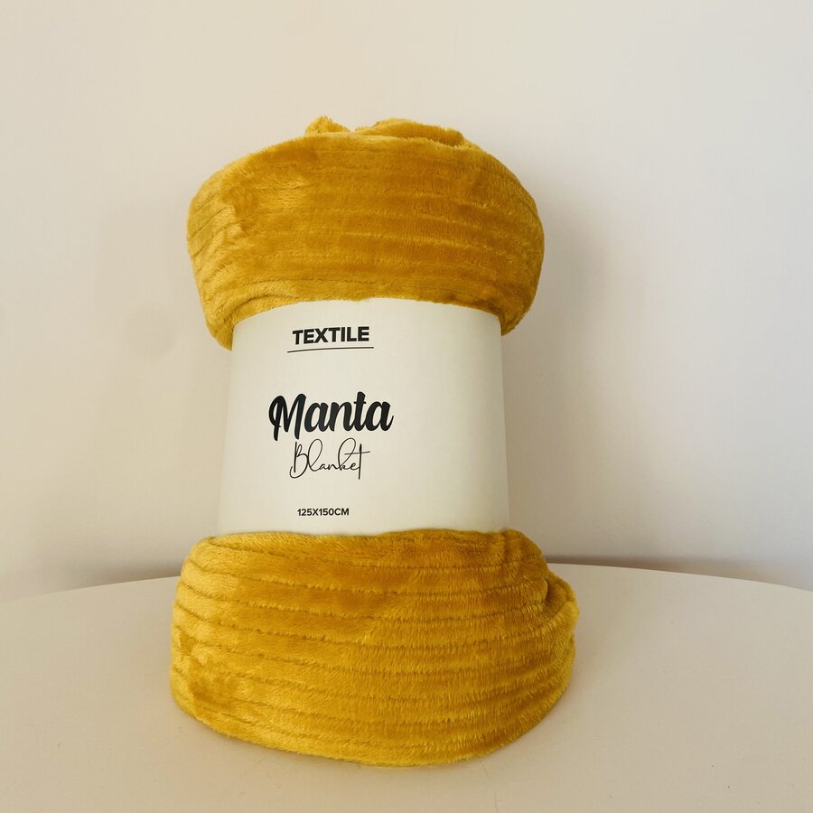 Manta amarela mostarda com etiqueta branca e texto, sobre superfície branca.