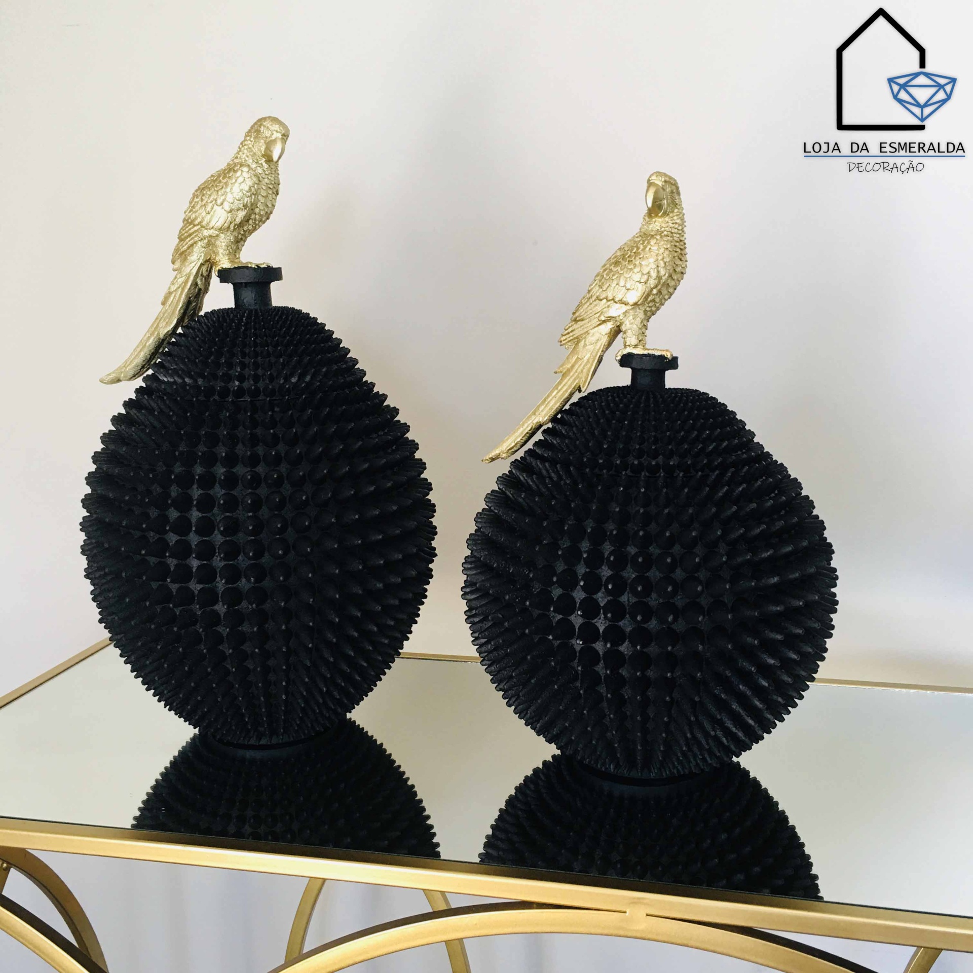 Dois jarros ovais pretos texturizados com pássaros dourados em cima sobre mesa espelhada com estrutura dourada