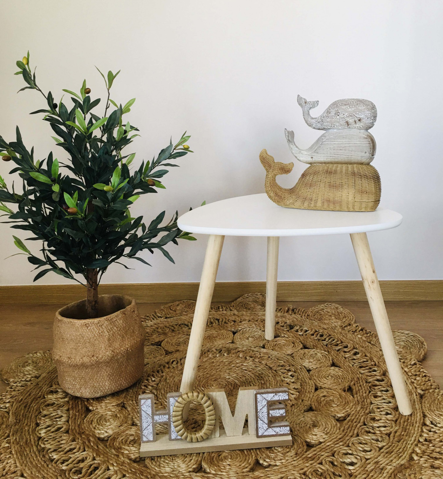 Conjunto decorativo com mesa branca, figuras de baleias de madeira, tapete de fibras naturais, planta em vaso de juta e placa com a palavra LOVE