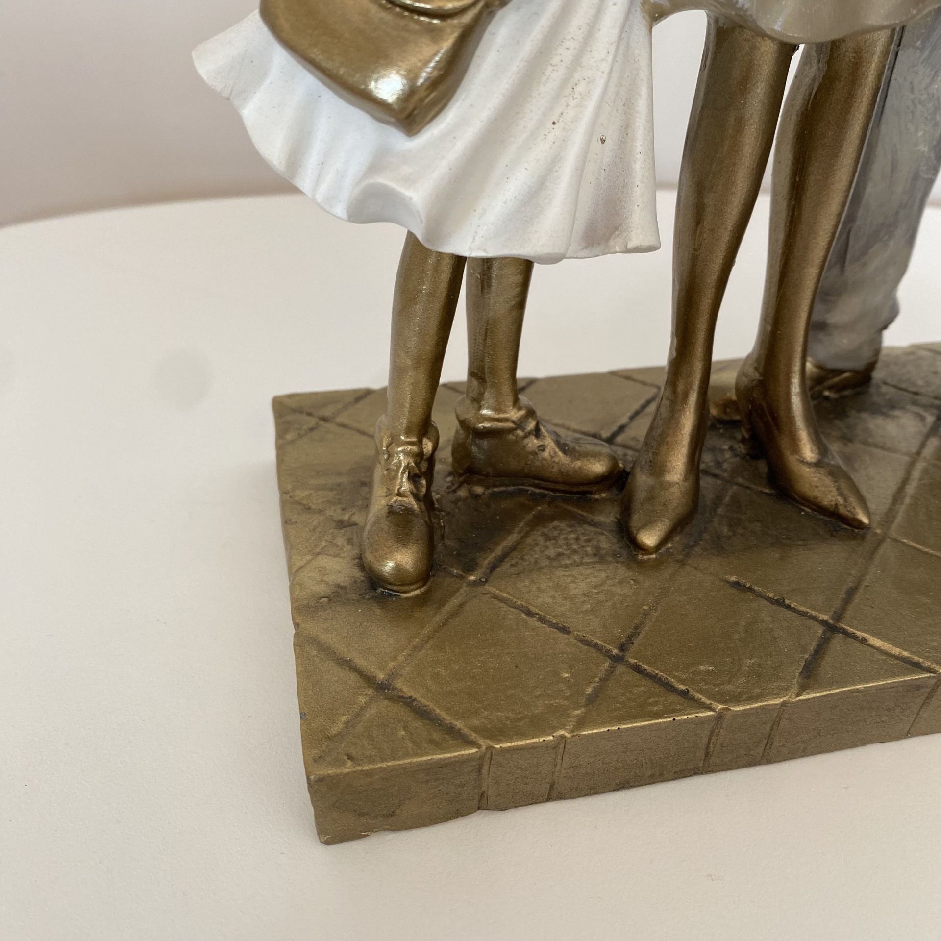 Estátua decorativa de pernas de figuras em dourado e branco sobre base com padrão