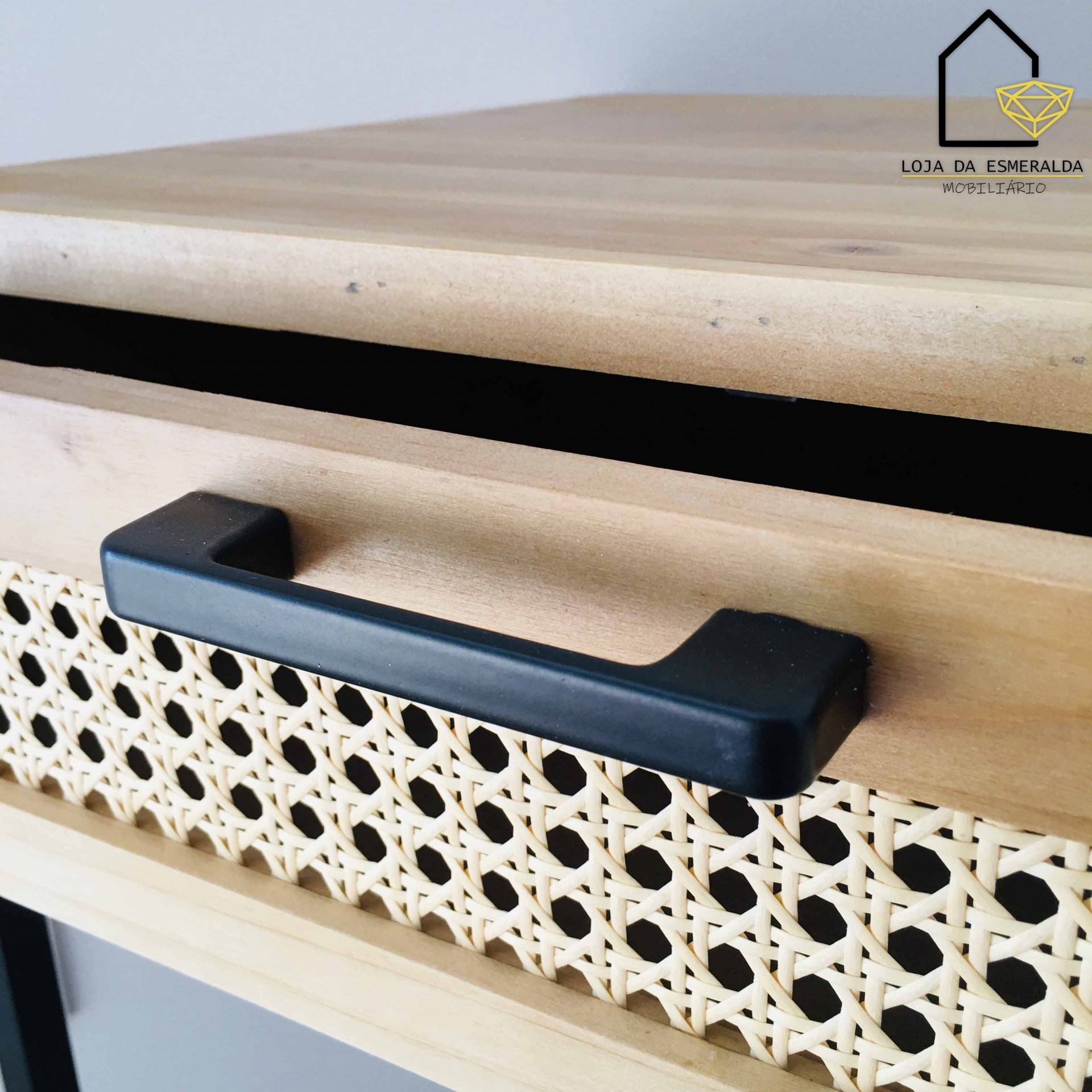 Cômoda em madeira clara com puxador preto e detalhe em vime entrelaçado.