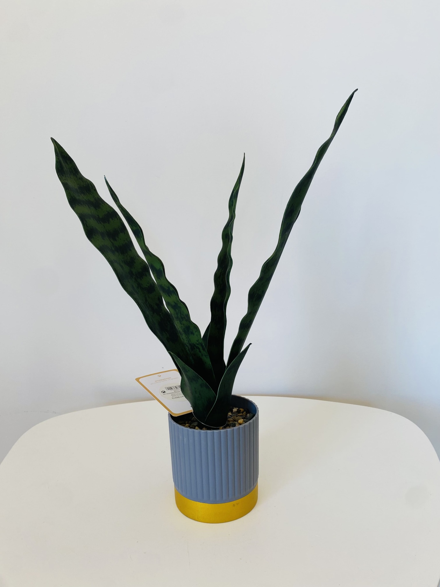 Planta artificial em vaso cinzento e dourado sobre mesa branca