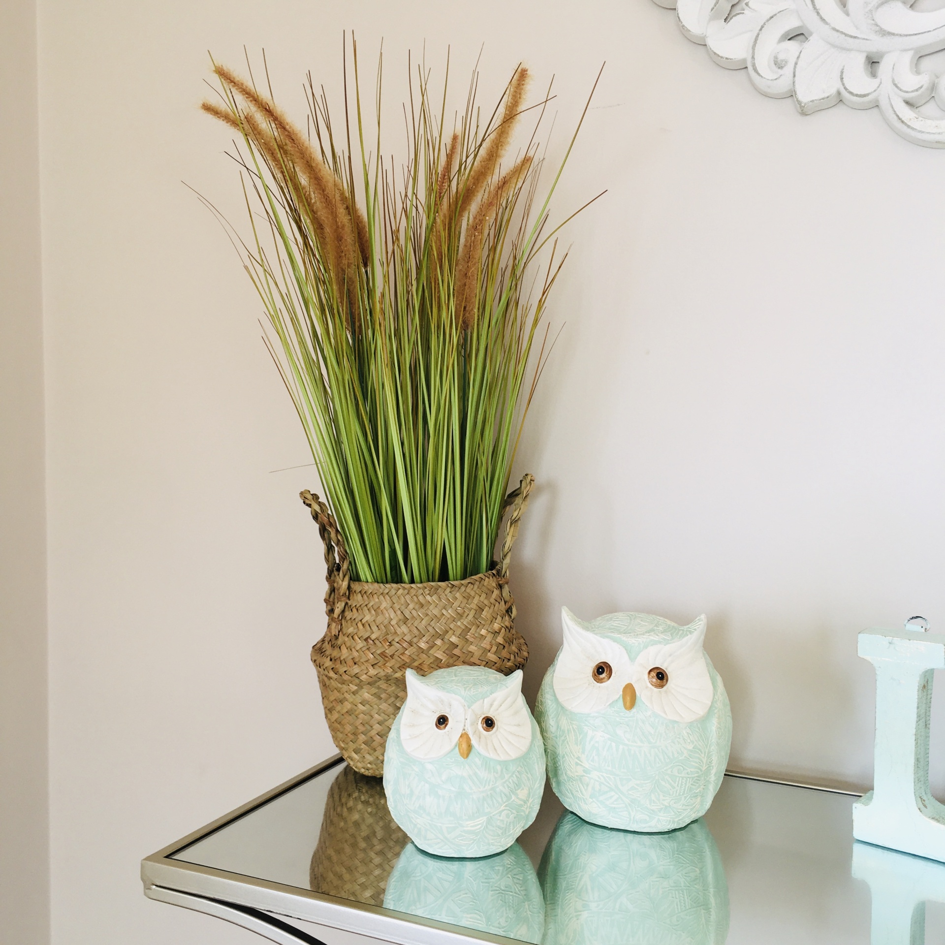 Duas corujas decorativas verdes e vaso trançado com plantas sobre mesa espelhada