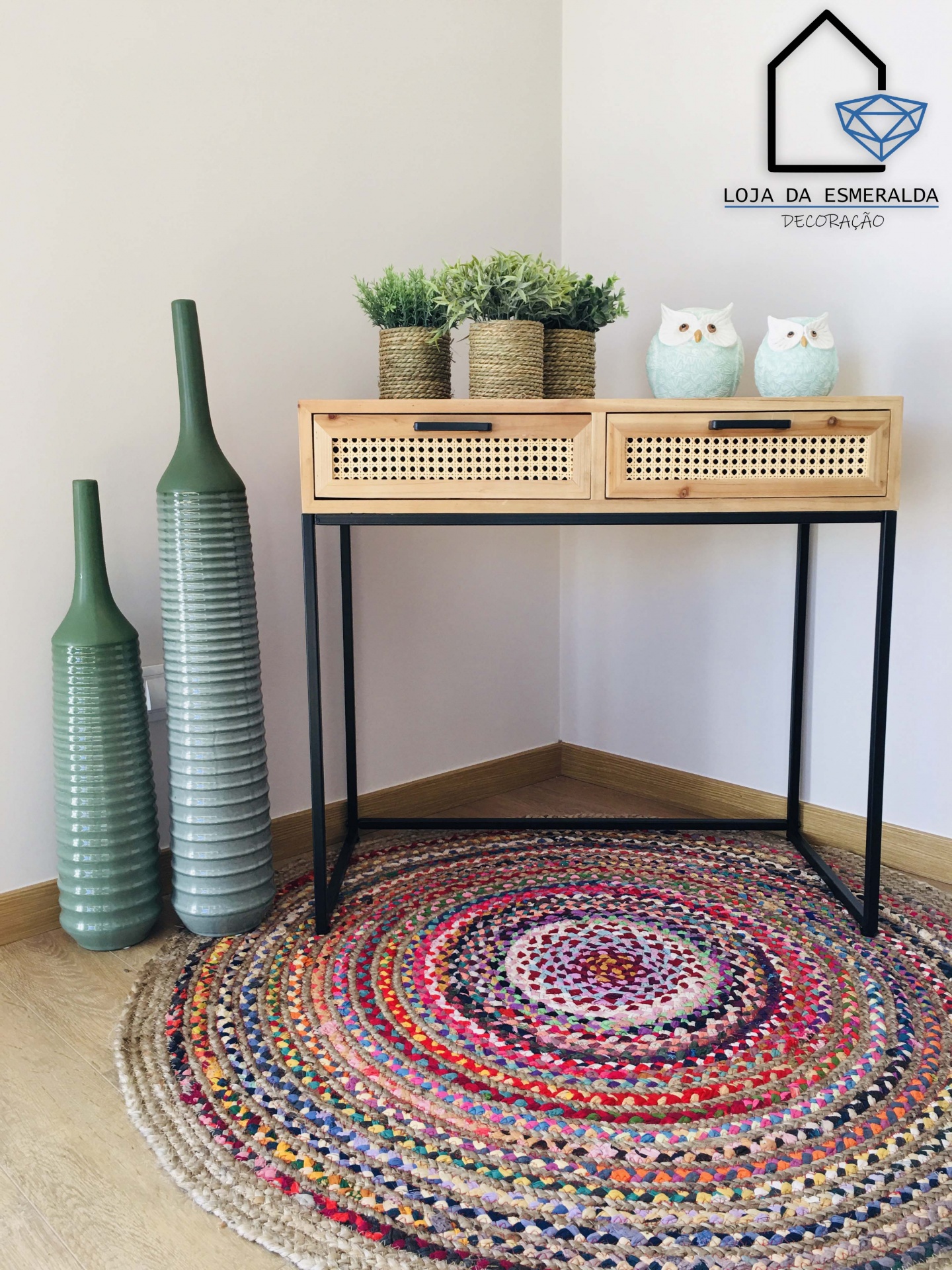 Aparador de madeira clara com gavetas de palhinha e decoração em canto com vasos e corujas em tapete redondo colorido