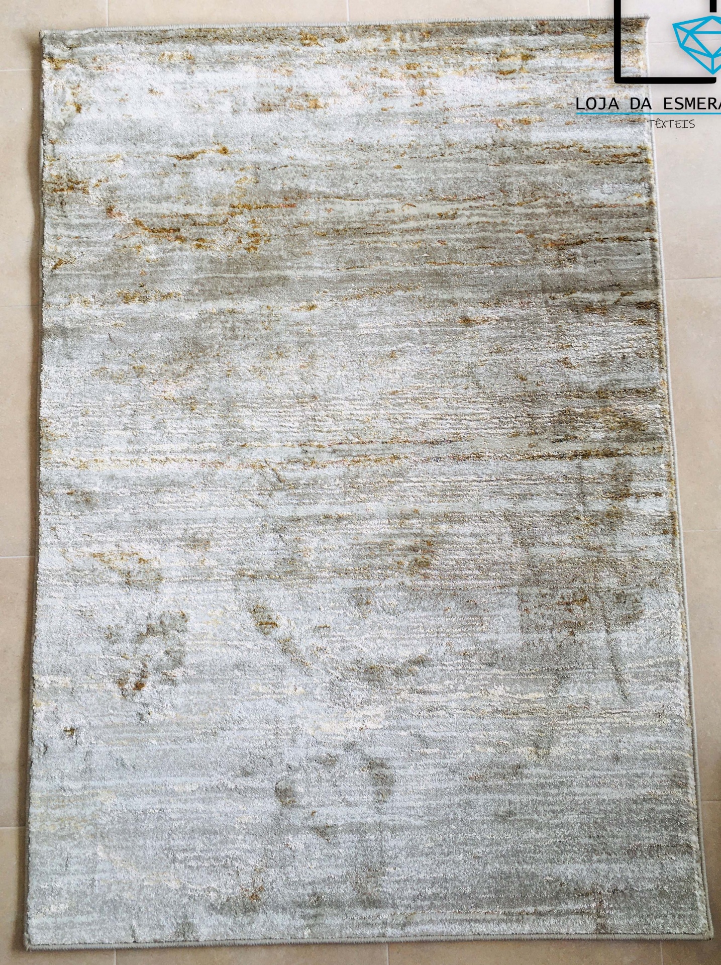 Tapete retangular cinza claro e bege com padrão abstrato colocado sobre chão de azulejos claros