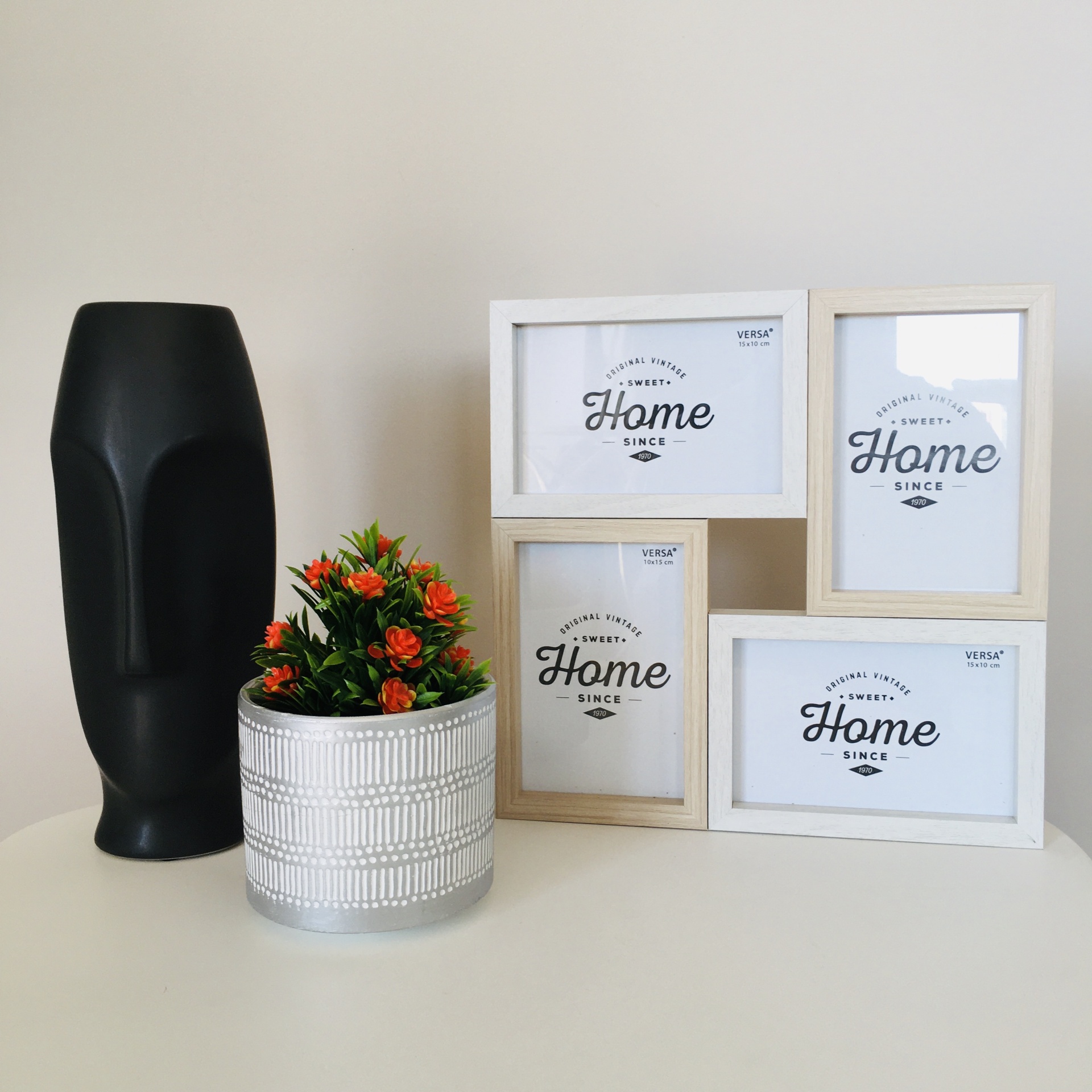 Molduras de fotos de madeira clara, vaso com planta e escultura preta