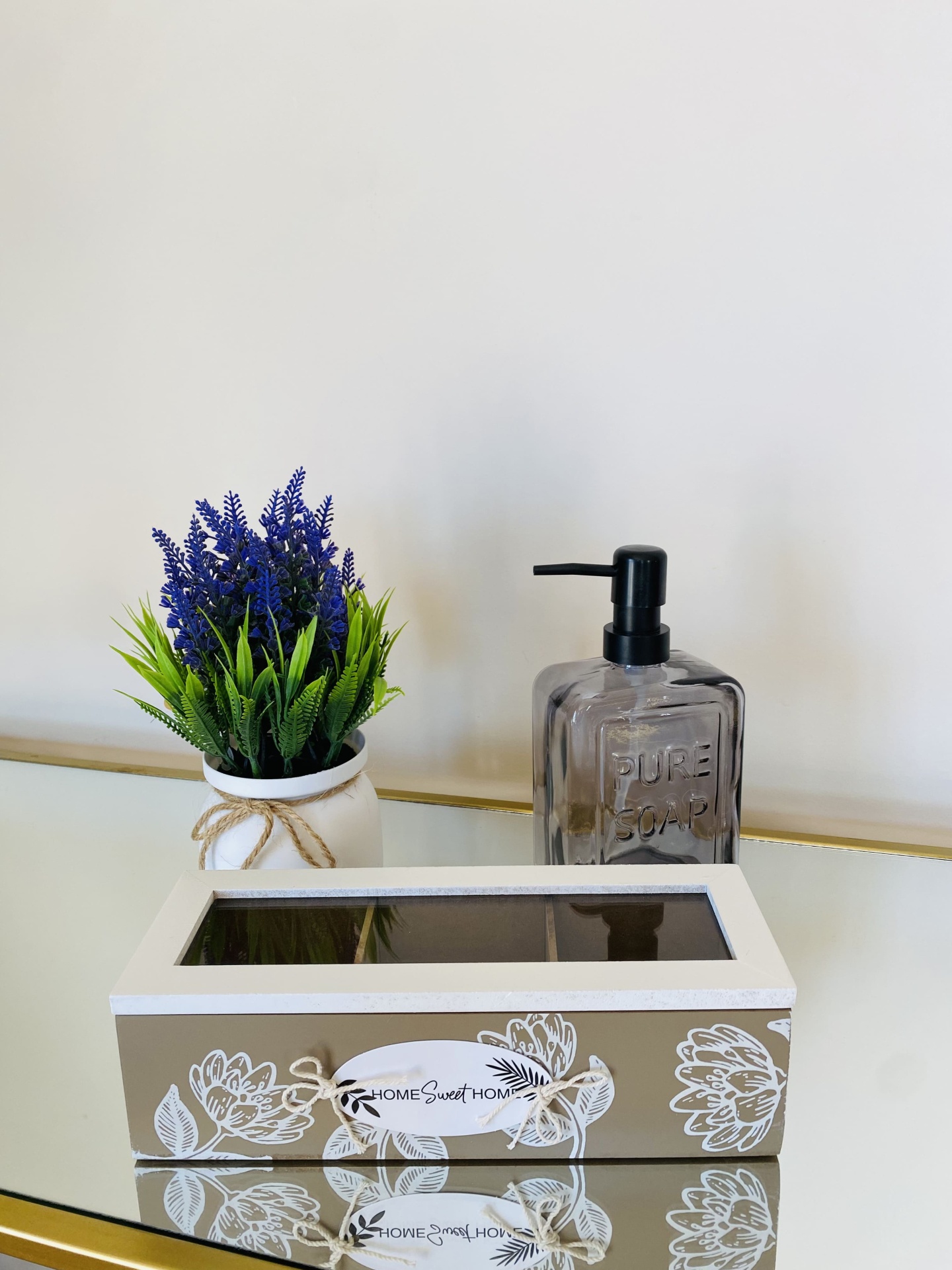 Caixa decorativa bege com padrão floral branco ao lado de planta artificial e frasco sabonete líquido cinza
