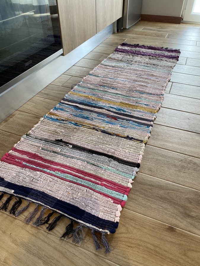 Tapete corredor colorido com riscas irregulares e franjas, colocado num chão de madeira junto a móveis de cozinha