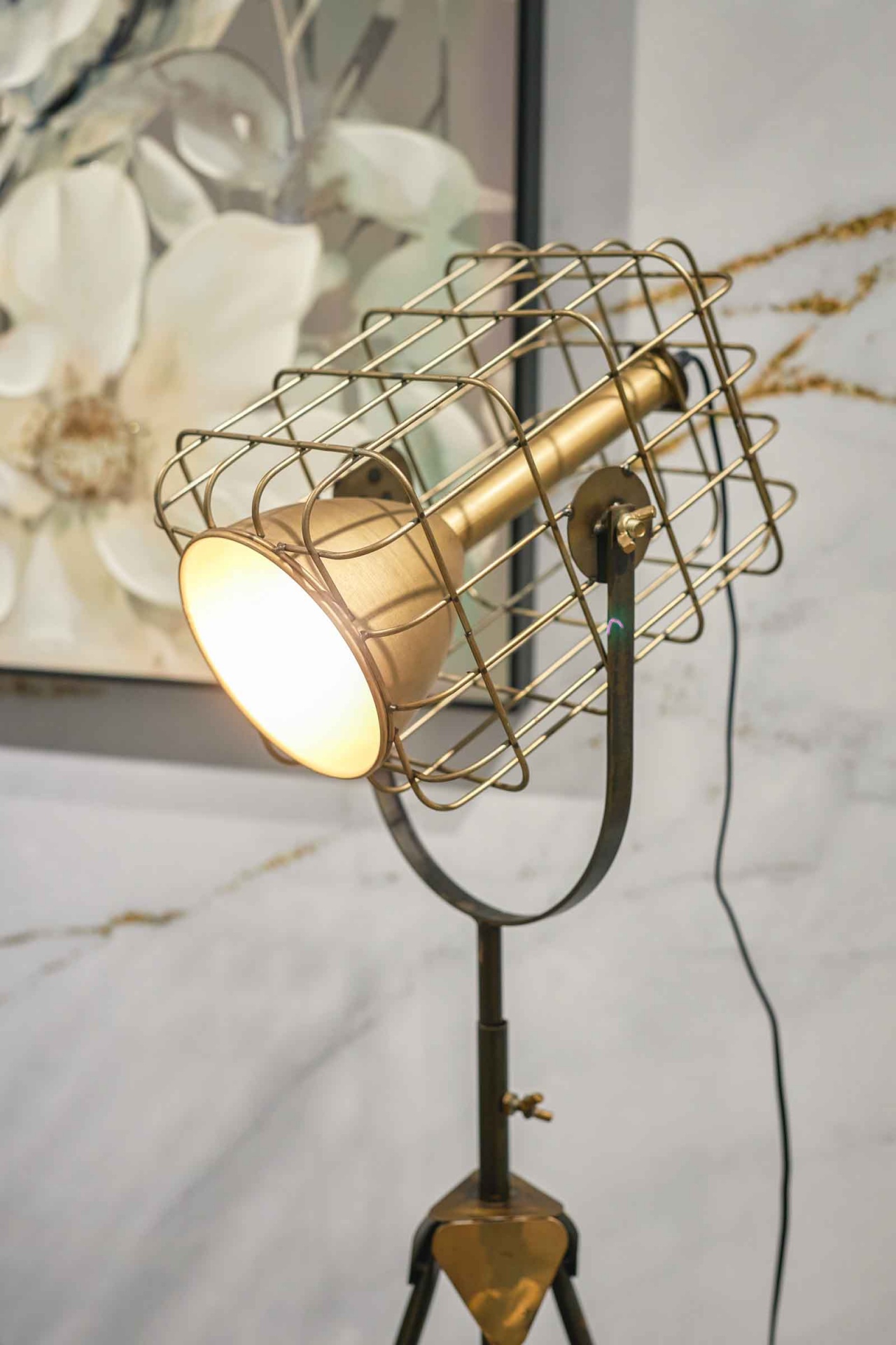 Candeeiro de pé industrial com gaiola metálica dourada e tripé preto, em ambiente interior