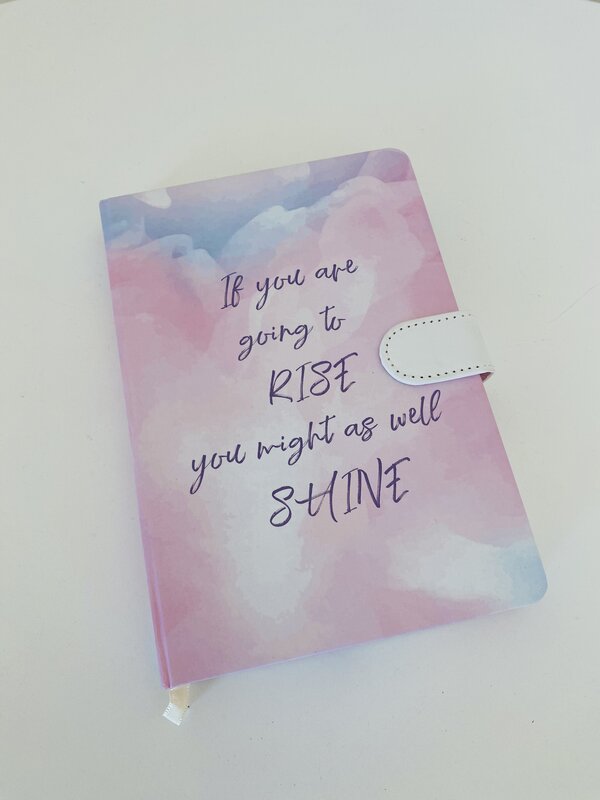 Caderno cor-de-rosa e azul com texto inspirador e fecho branco