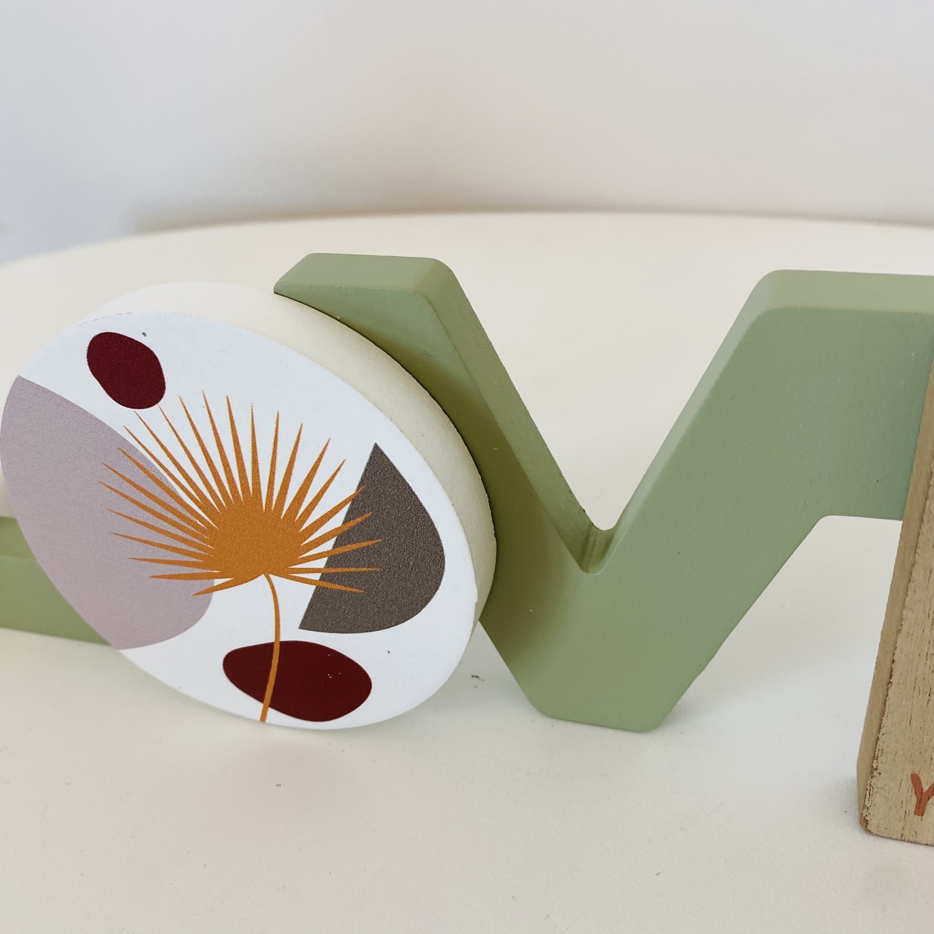 Peça decorativa em madeira verde e branca com padrão gráfico de folhas em tons castanhos