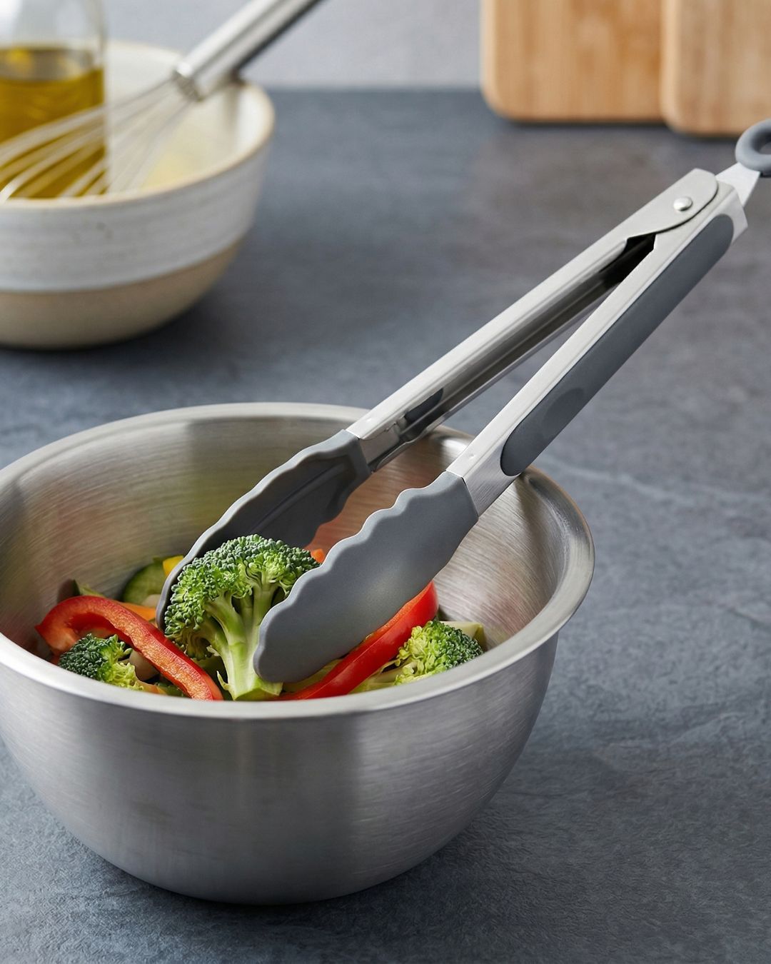 Pegador metálico e silicone cinzento numa tigela de inox com vegetais frescos em bancada cinzenta