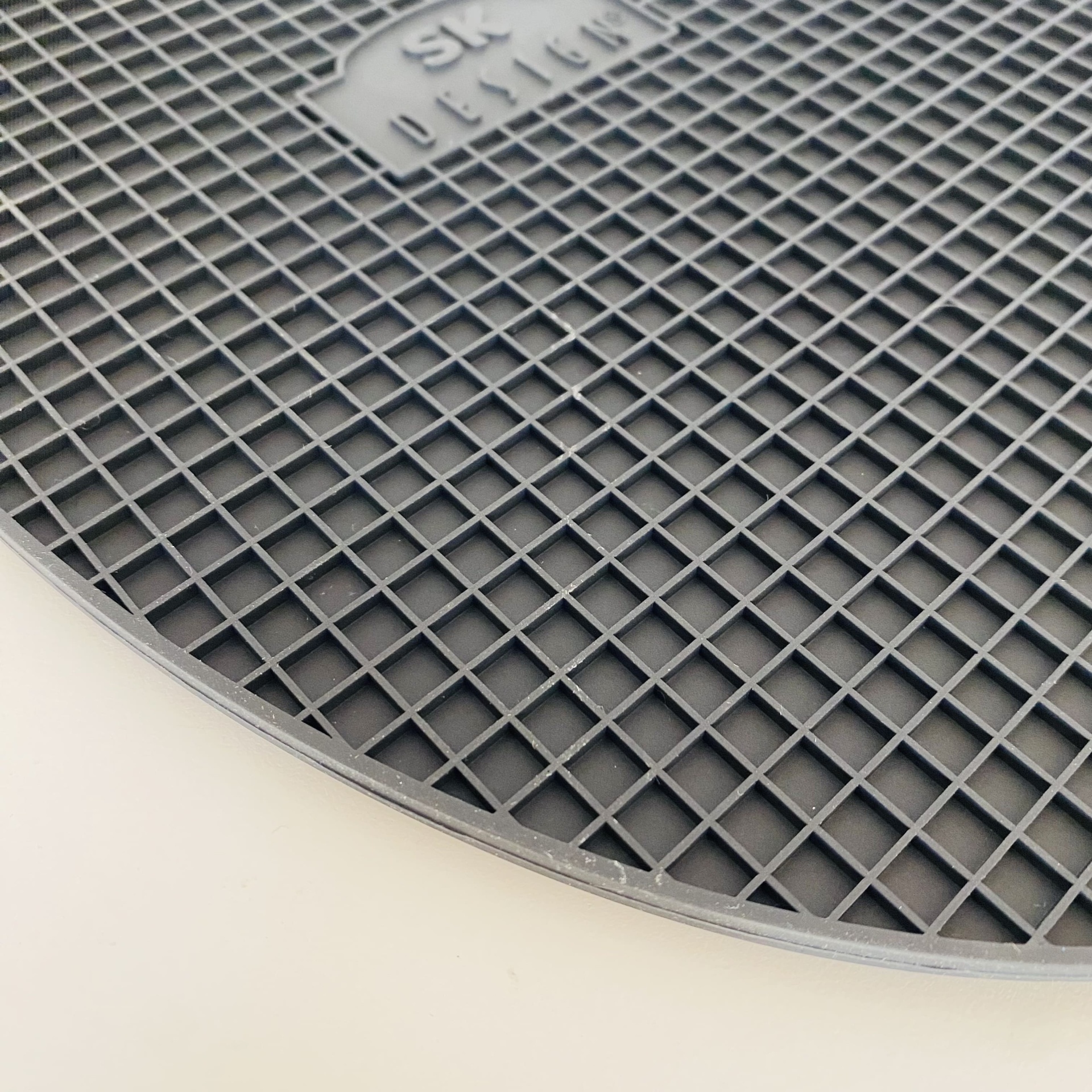 Tampa redonda de plástico cinzento com padrão em grelha e texto SK DETAIL em relevo