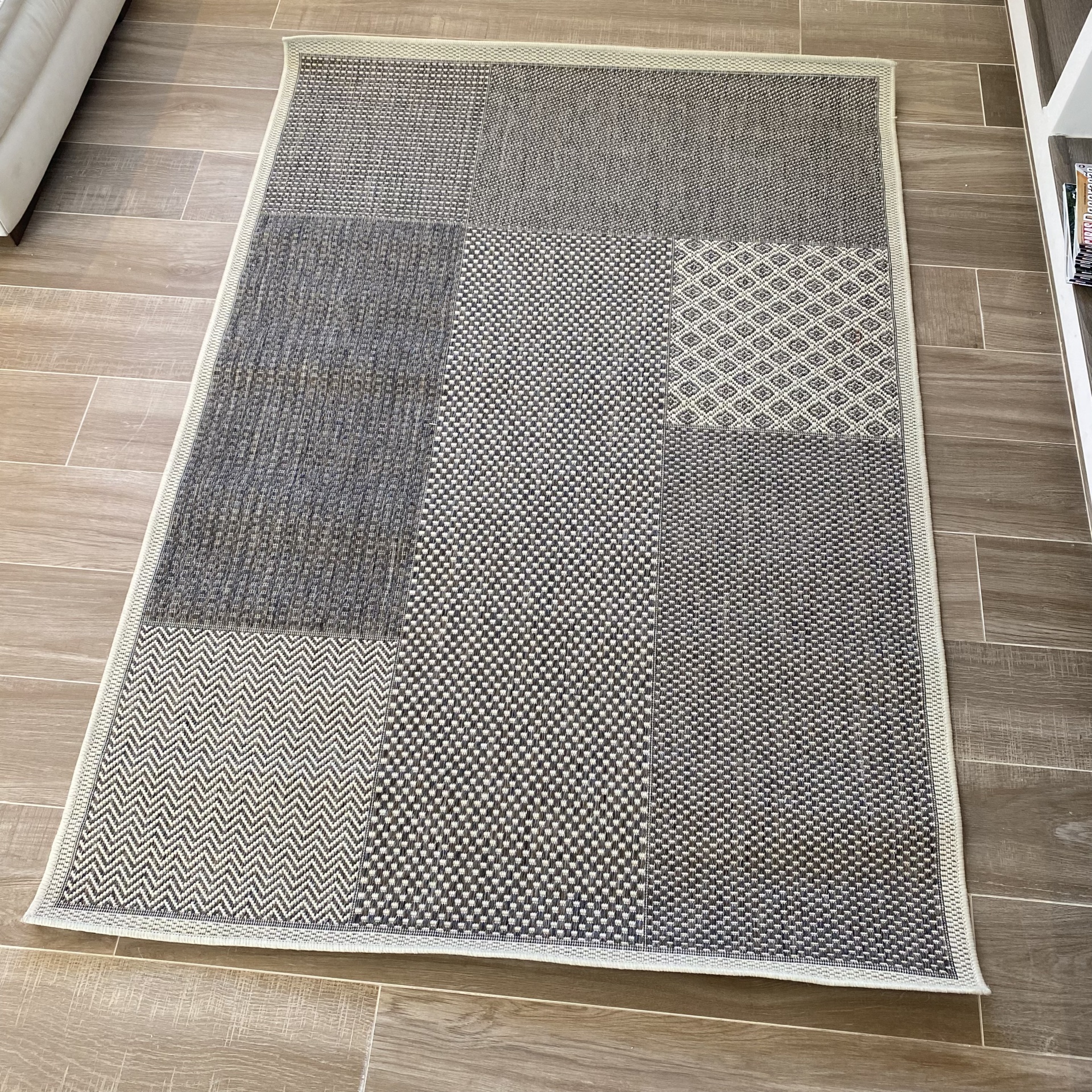 Tapete com padrões geométricos em cinza e bege no chão de pedra castanho claro ao lado de sofá branco