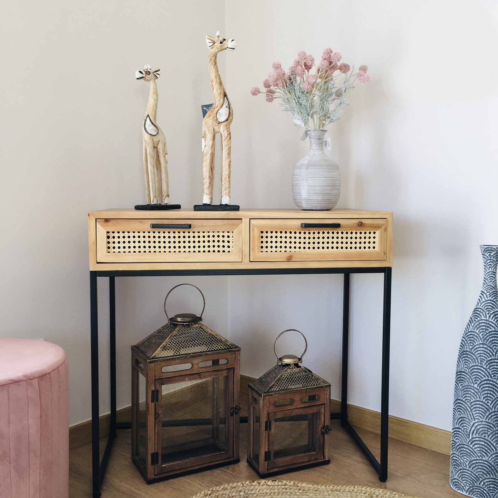 Consola em madeira clara com gavetas em palhinha, esculturas de girafa, vaso com flores e lanternas metálicas