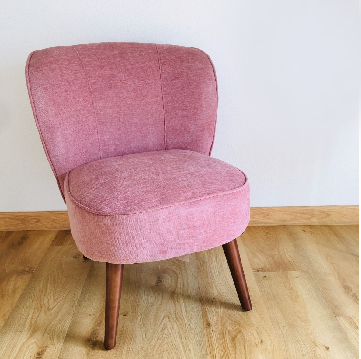 Cadeira cor de rosa com pernas de madeira numa sala com chão de madeira clara
