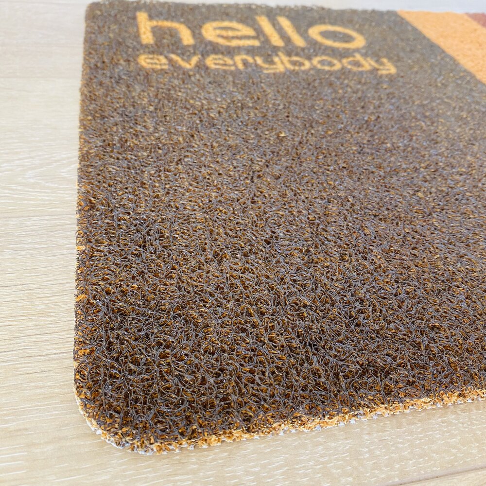 Tapete castanho com texto amarelo 'hello everybody' sobre chão de madeira clara