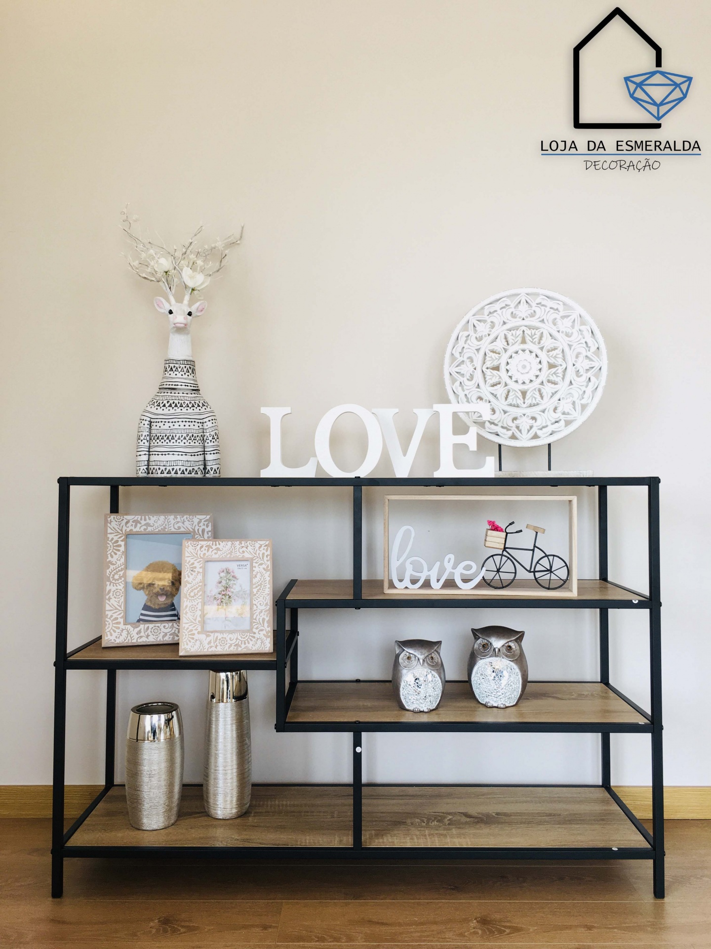 Aparador decorado com objetos em madeira, metal e cerâmica, com logo Loja da Esmeralda Decoração ao fundo