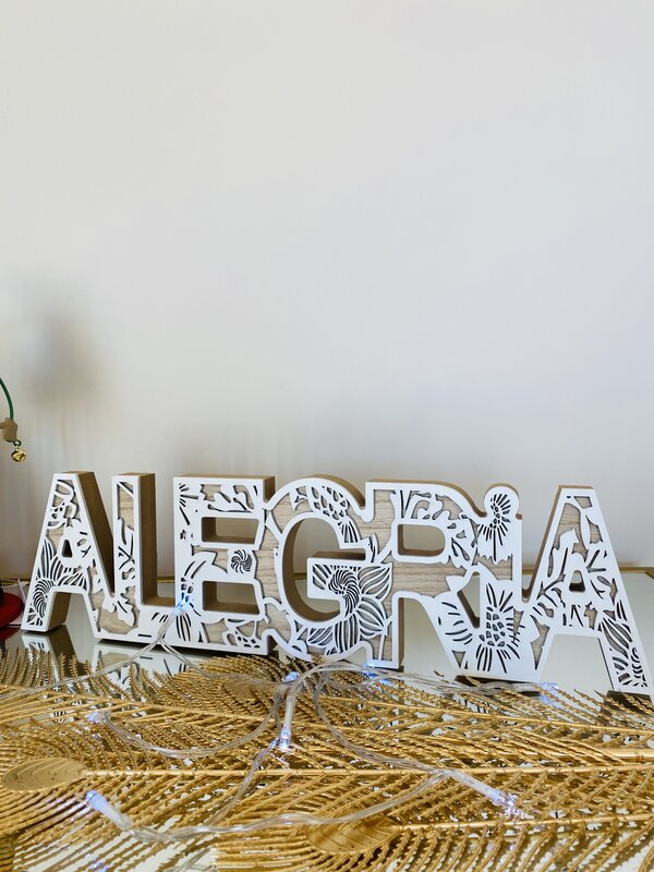 Decoração de mesa em letras de madeira recortadas com padrão floral branco e bege formando a palavra ALEGRIA