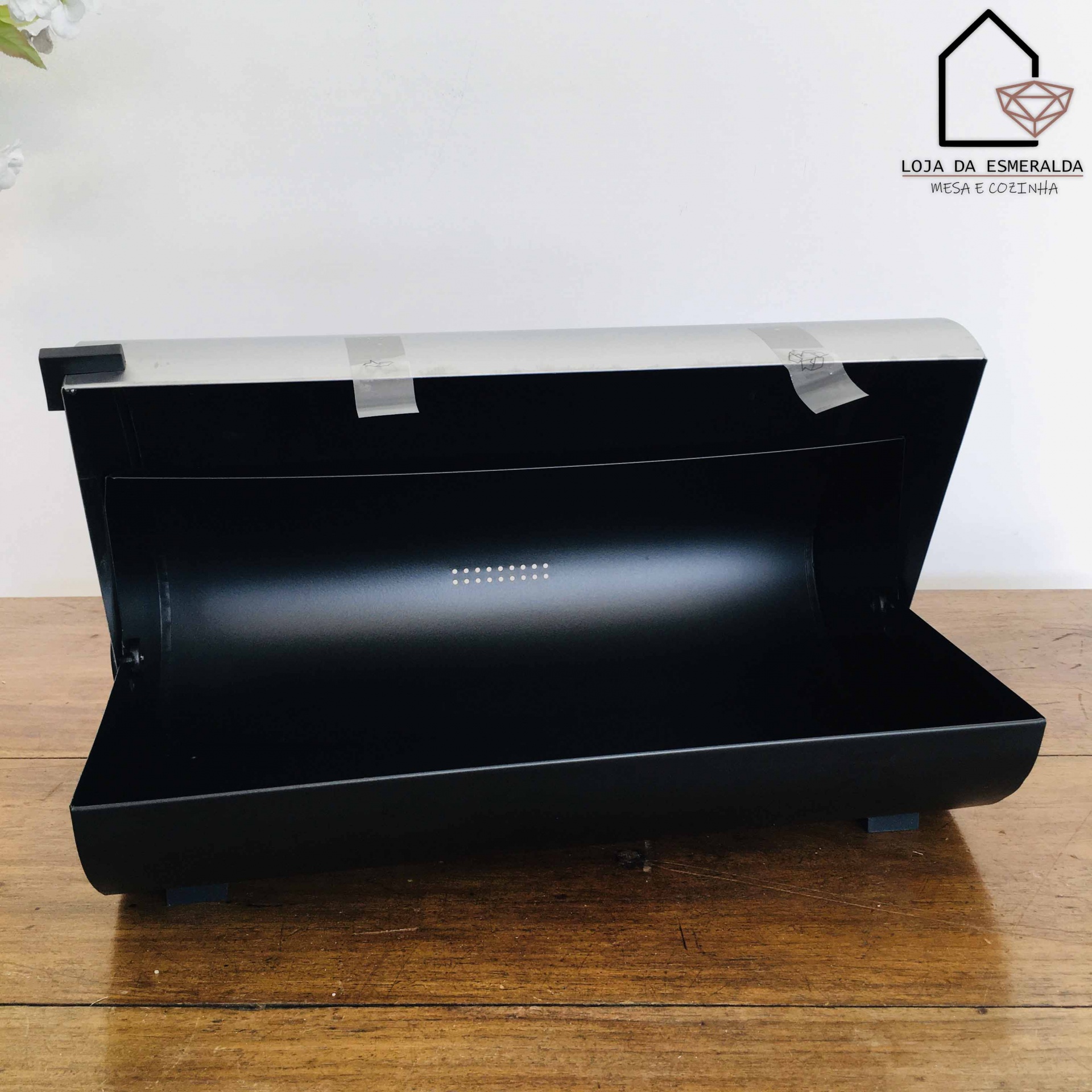 Caixa preta retangular de metal com tampa aberta sobre mesa de madeira