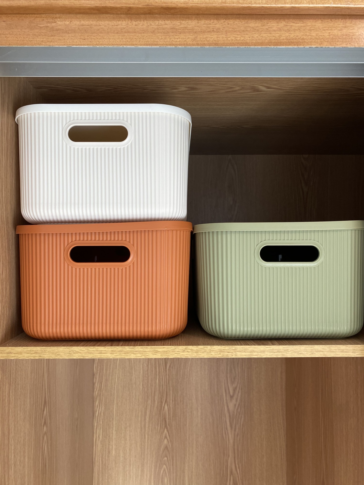 Caixas organizadoras brancas, terracota e verdes numa prateleira de madeira