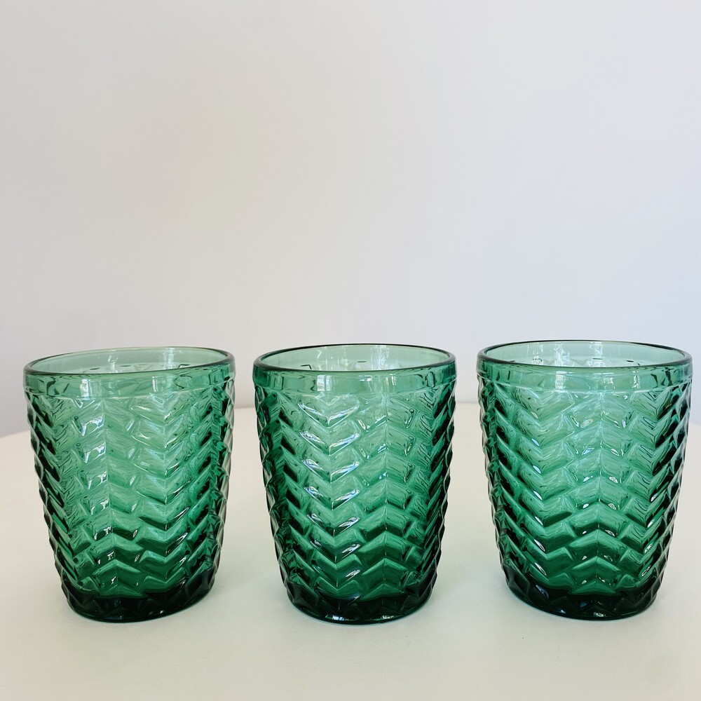 Três copos verdes em vidro com padrão em relevo sobre superfície branca
