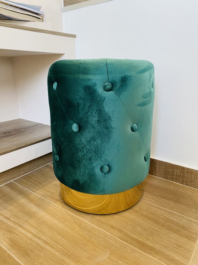 pufe verde aveludado redondo com base em madeira clara em chão de madeira ao lado de secretária branca
