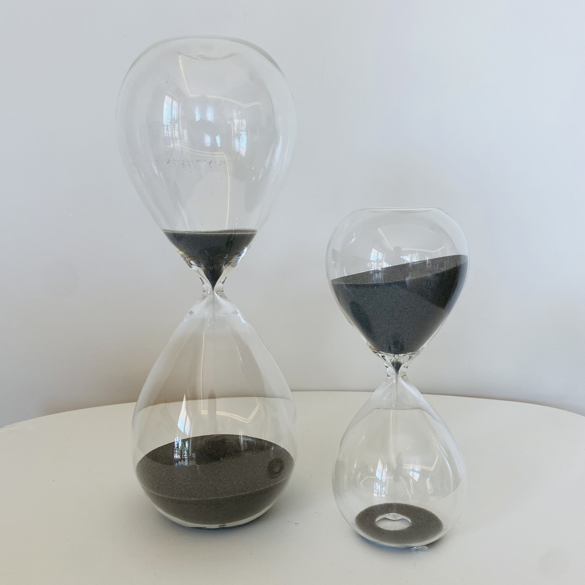 Duas ampulhetas de vidro com areia preta sobre uma mesa branca