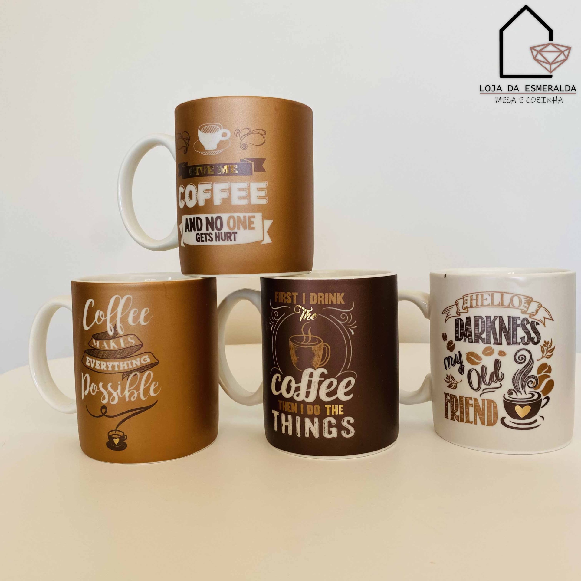 Quatro canecas de café em tons castanho e branco com frases engraçadas em inglês, dispostas em superfície clara.