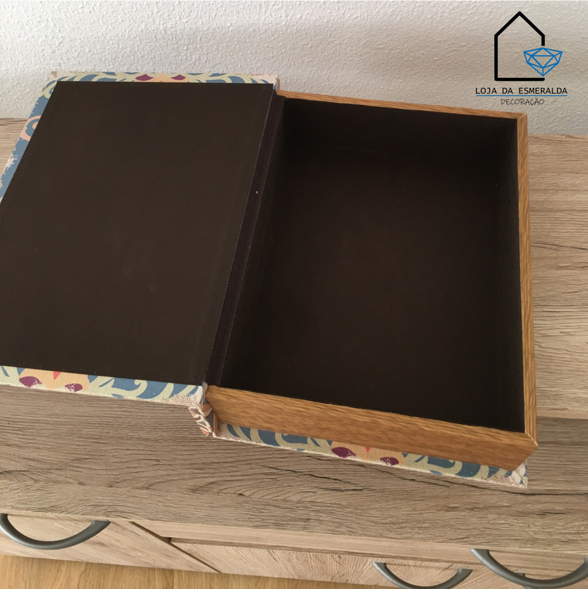 Caixa de arrumação floral com interior castanho aberta sobre móvel de madeira clara