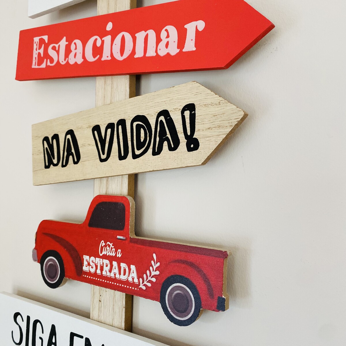 Placa decorativa de madeira com setas vermelha, bege e branca com textos e uma camionete vermelha