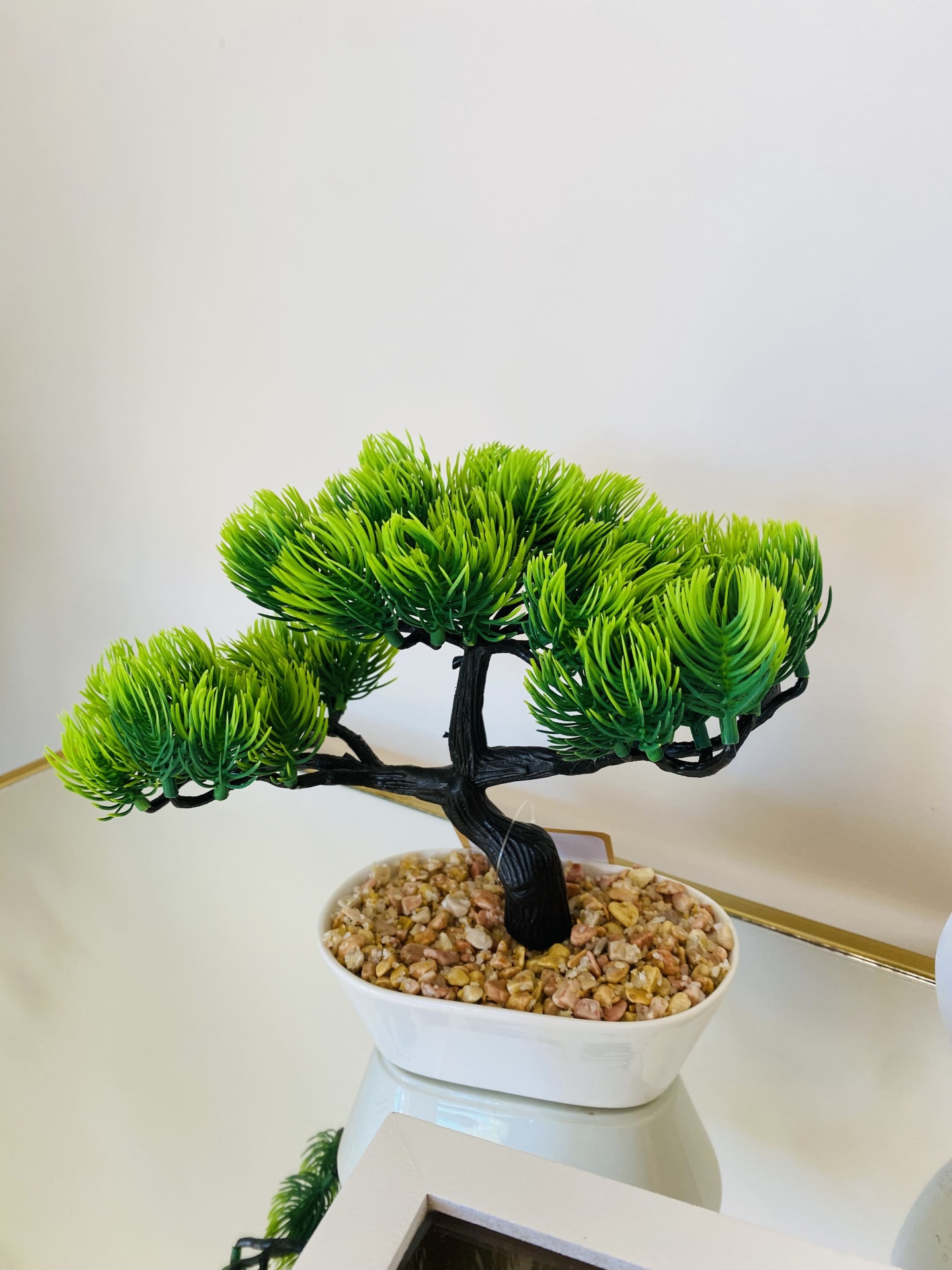 Bonsai artificial com folhas verdes num vaso branco com pedras