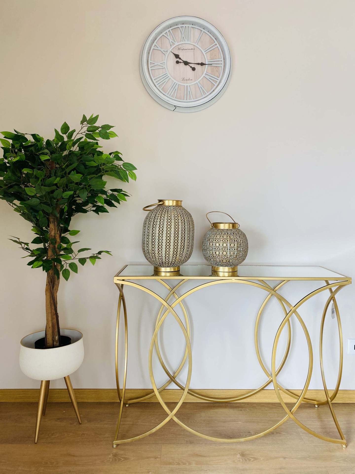 Relógio de parede, mesa dourada, vasos decorativos e planta artificial numa sala