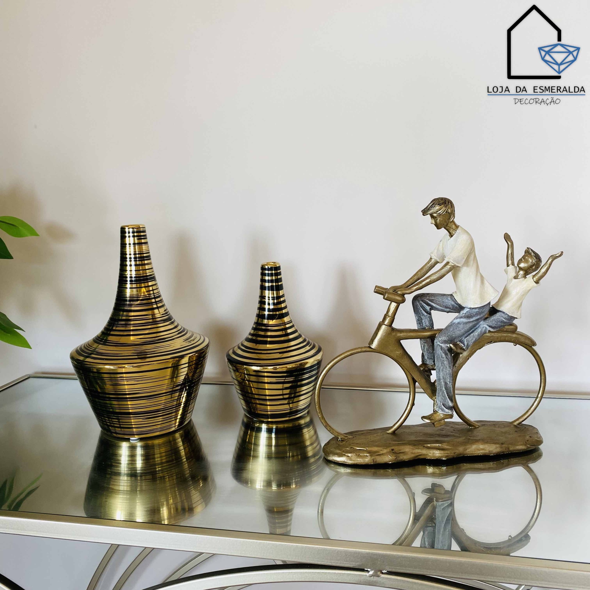 Vasos decorativos dourados e pretos e escultura de homem e criança numa bicicleta sobre mesa espelhada