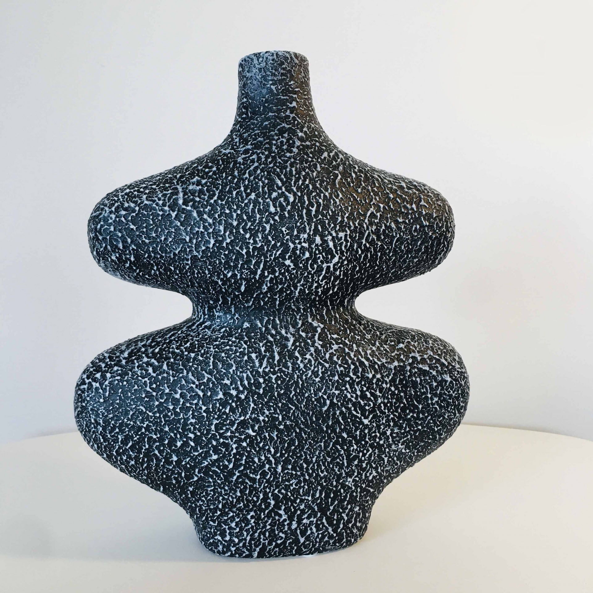 Vaso decorativo preto com manchas brancas em superfície branca