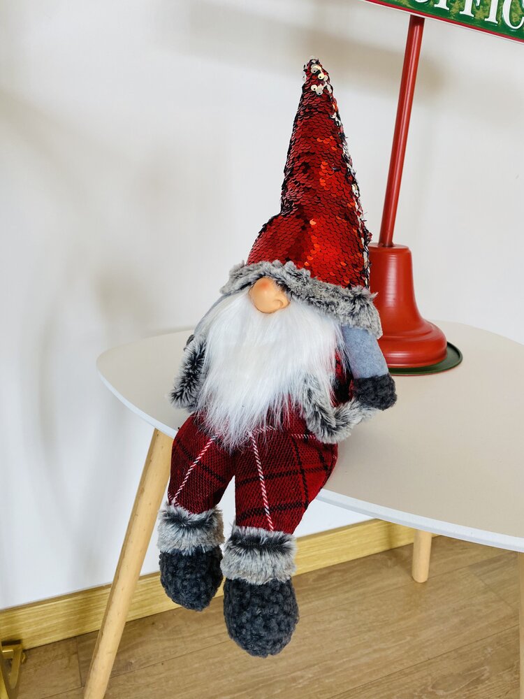 Boneco decorativo de Natal com gorrinho vermelho e barba branca sentado numa mesa branca.