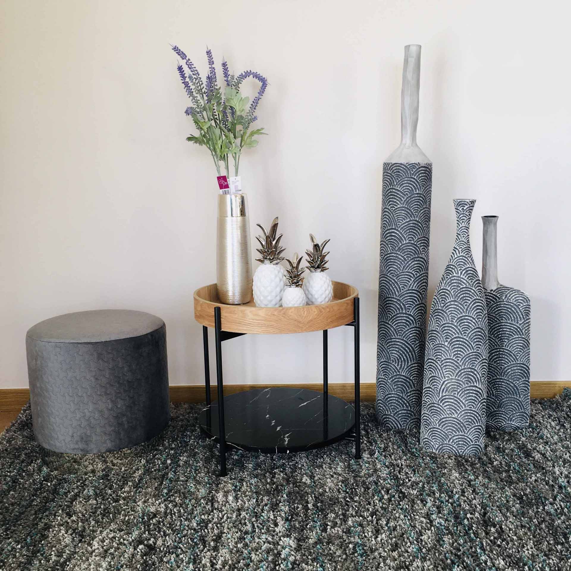 Conjunto decorativo com tamborete, mesa auxiliar, vasos decorativos e flores sobre tapete cinzento