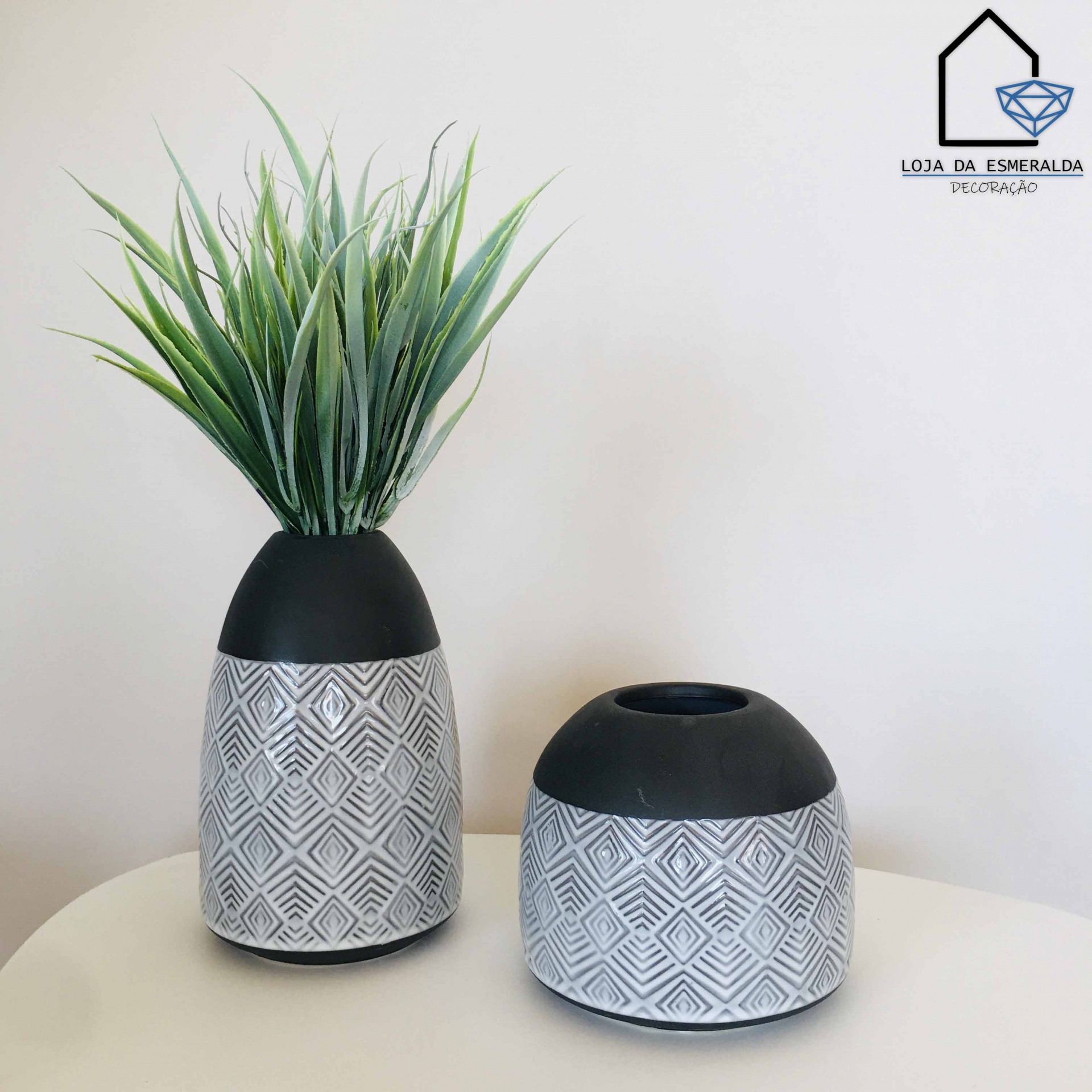 Dois vasos decorativos cinza e preto com padrão geométrico, um com planta artificial e outro vazio