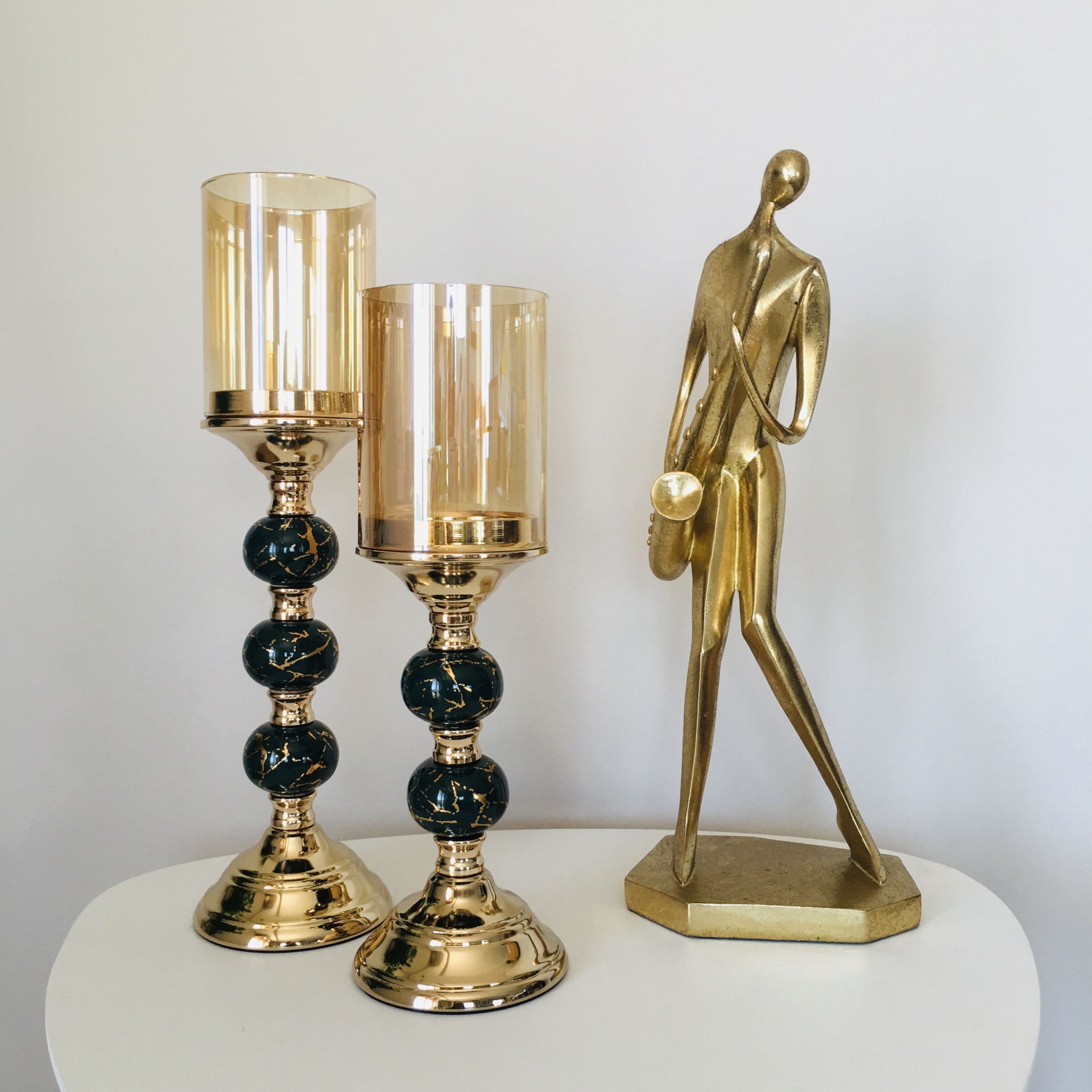 Conjunto de castiçais dourados com esferas pretas e vidro âmbar junto a uma escultura dourada abstrata de figura humana