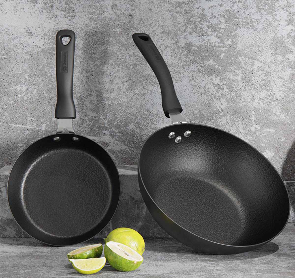 Dois tachos antiaderentes pretos com cabos pretos junto a limas e limões cortados