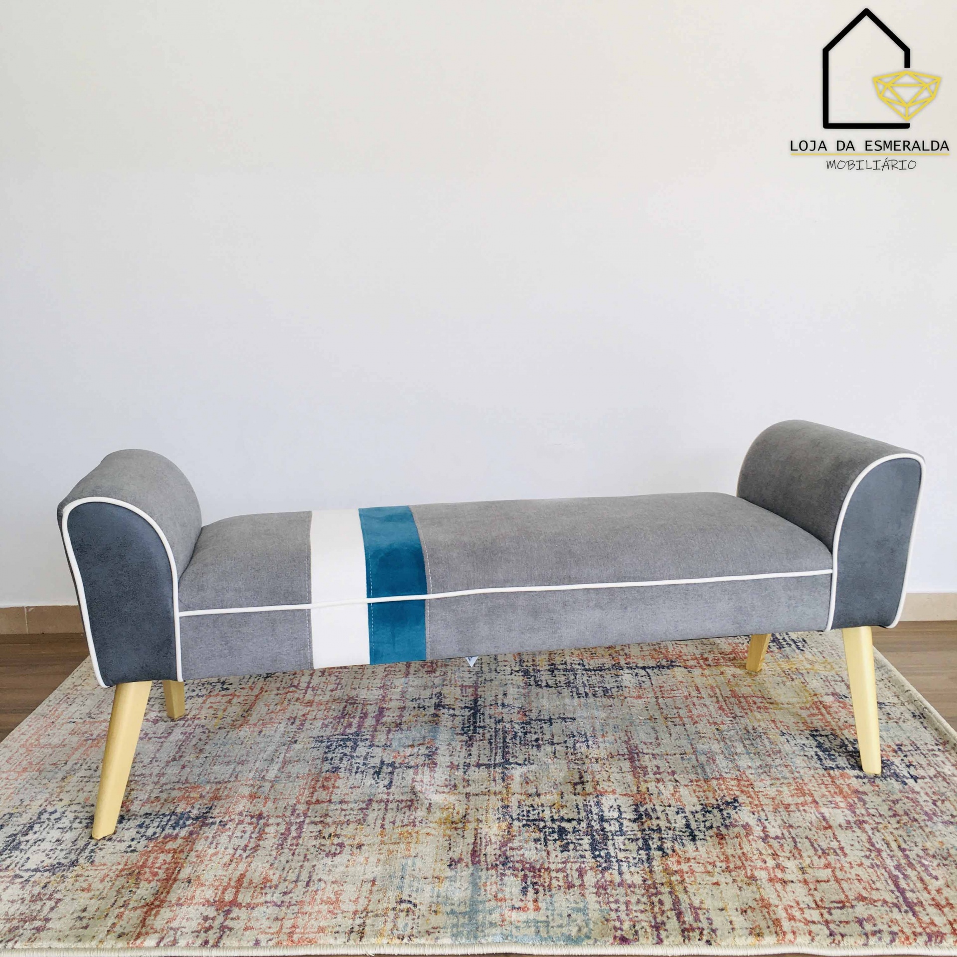 Banco estofado cinzento com detalhes em branco e azul e pernas de madeira sobre tapete colorido
