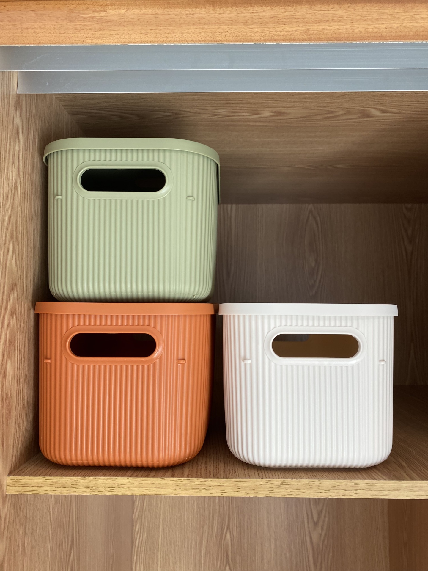 Três caixas de plástico coloridas em prateleira de madeira