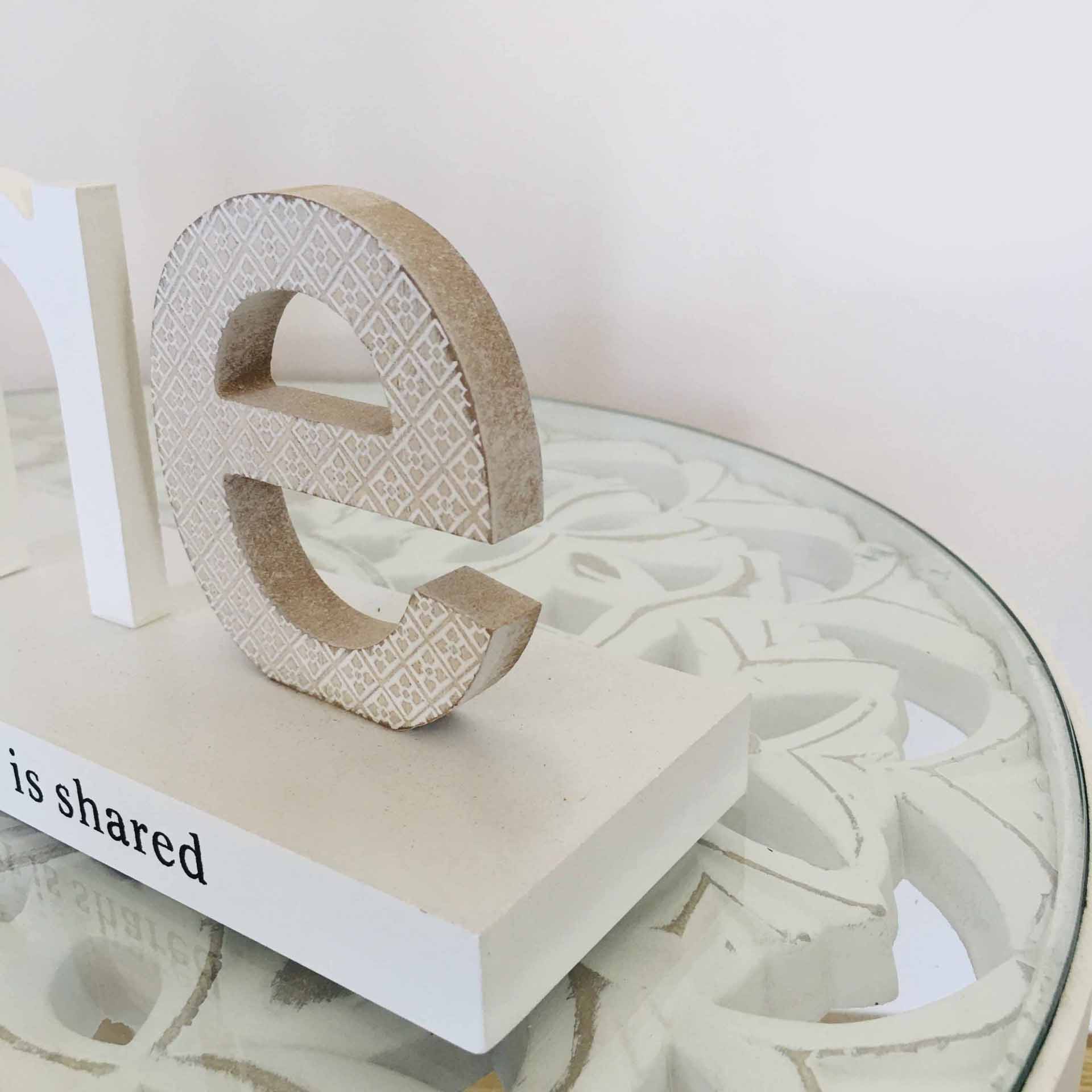 Escultura decorativa da letra 'e' em tom bege claro e branco sobre base branca com texto 'is shared' numa mesa de vidro redonda.