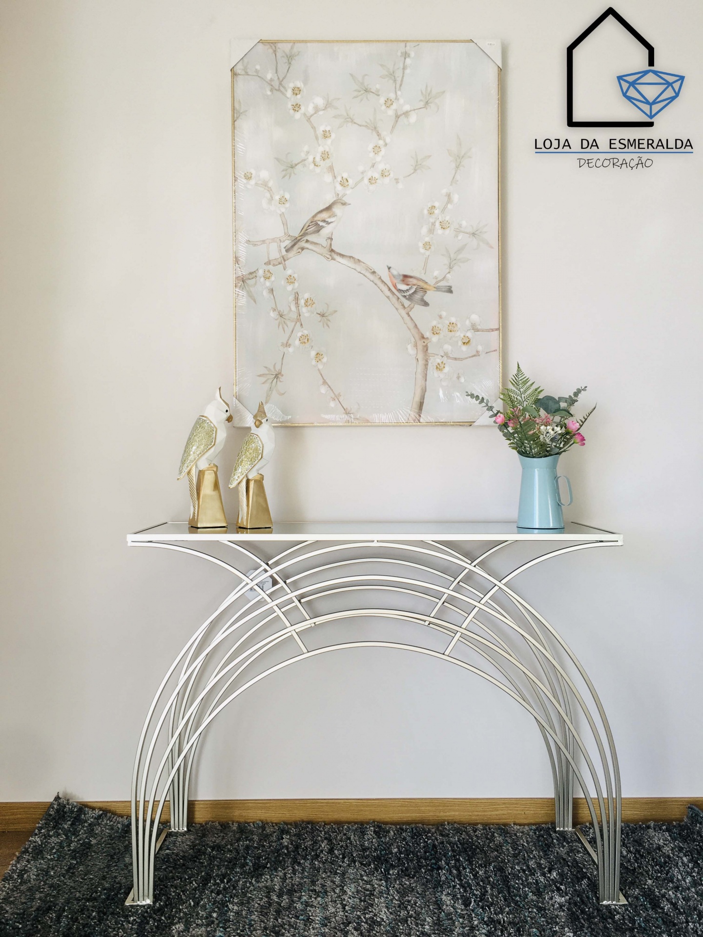 Mesa decorativa branca com pássaros dourados, vaso azul com flores e quadro com pintura de pássaros