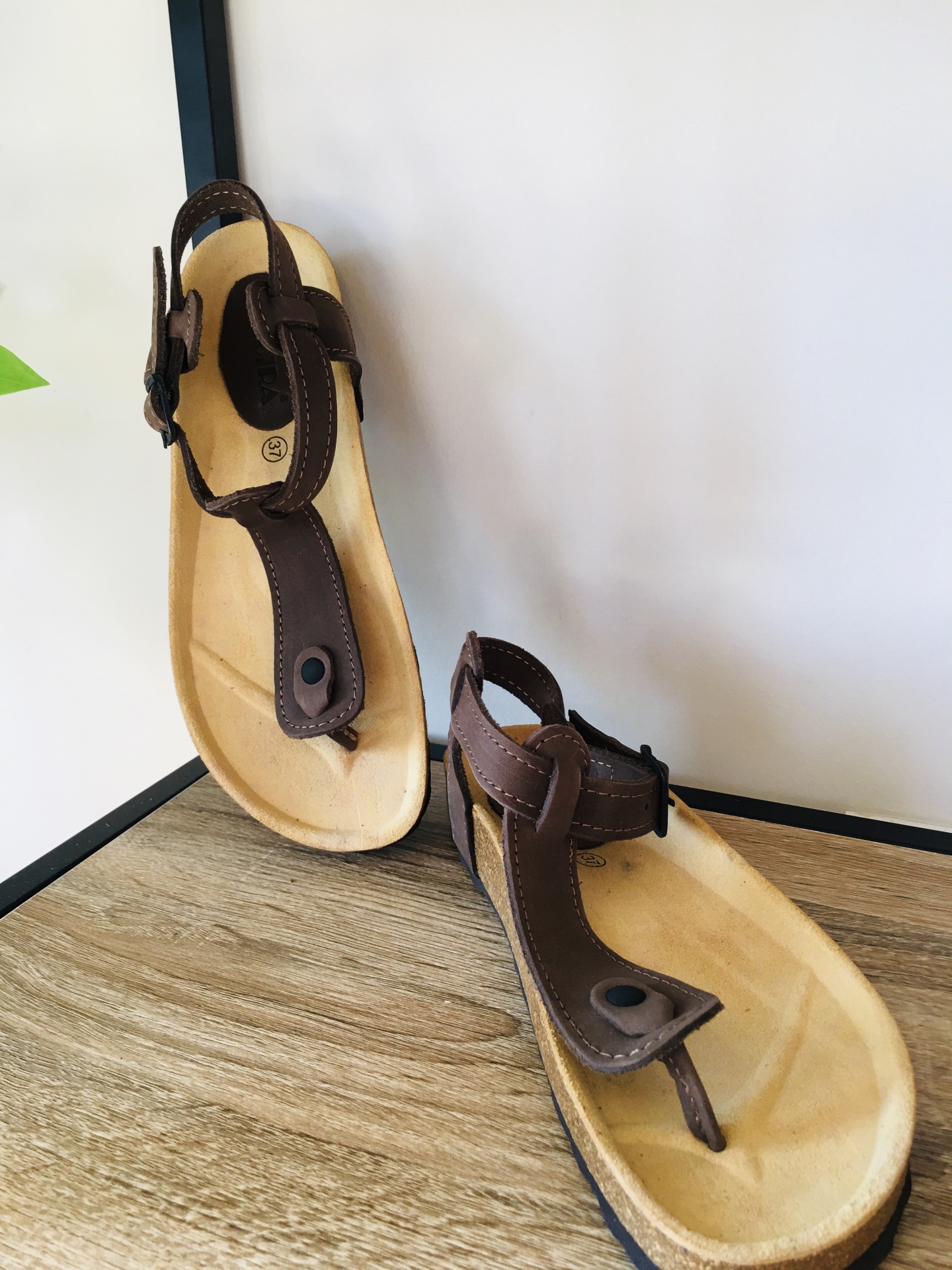 Sandálias castanhas com tiras em couro e sola clara sobre superfície de madeira.