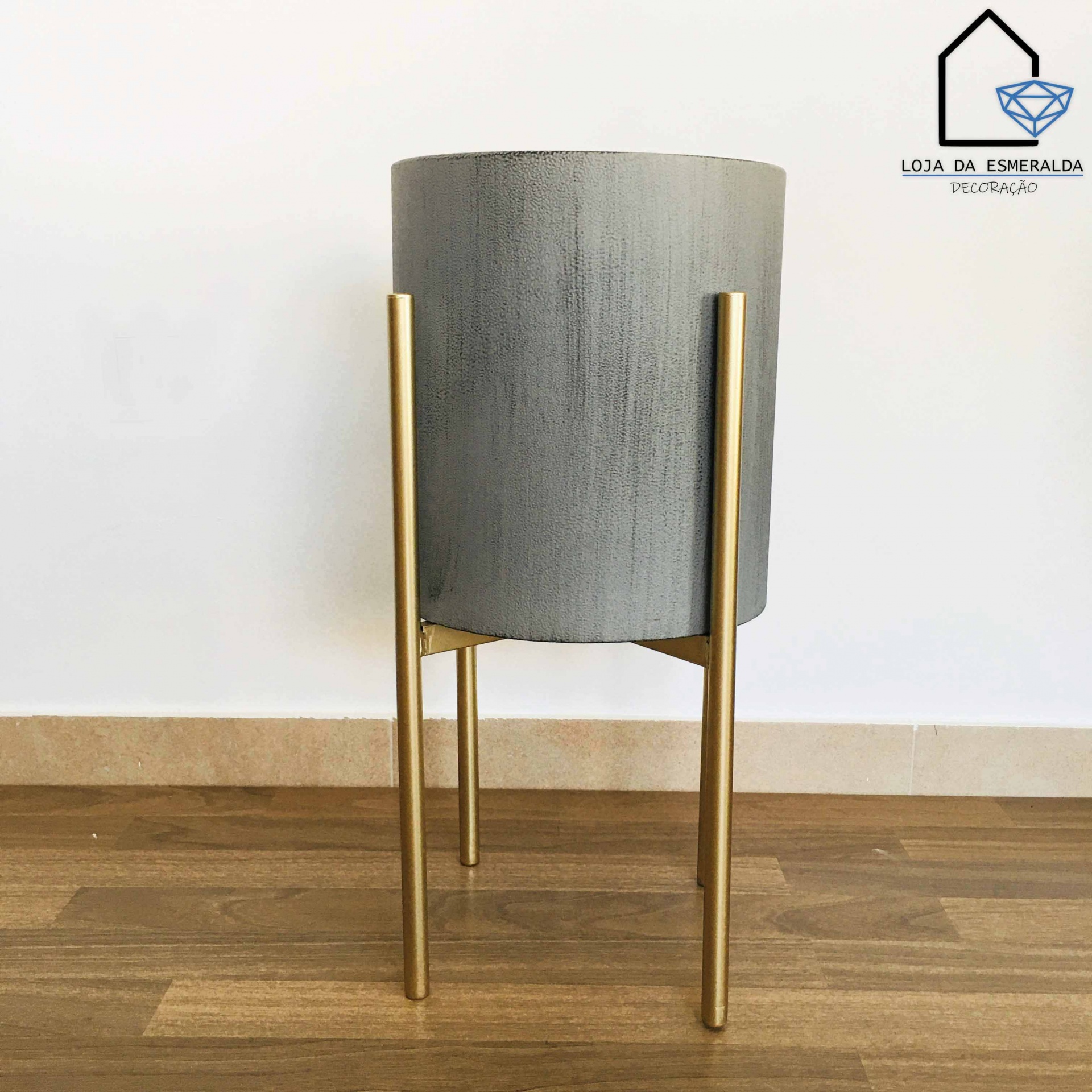 vaso cinzento com suporte metálico dourado em chão de madeira